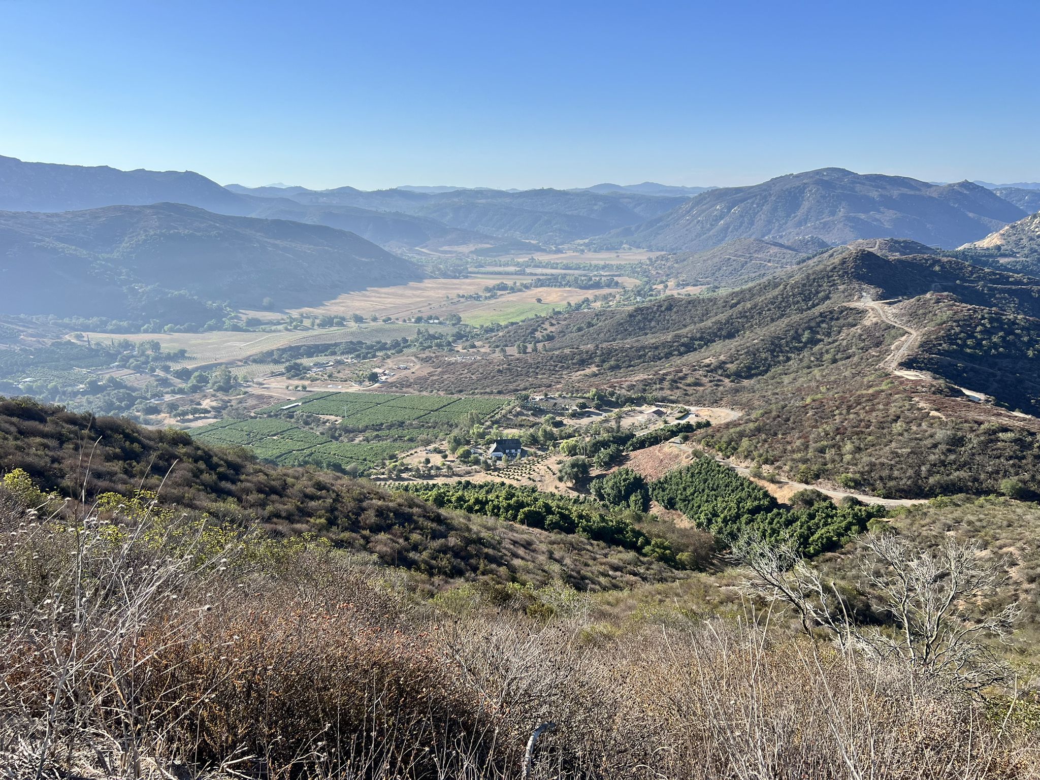 Expansive valley with green fields and distant mountains under a clear sky. - Monserate Mountain Loop Trail