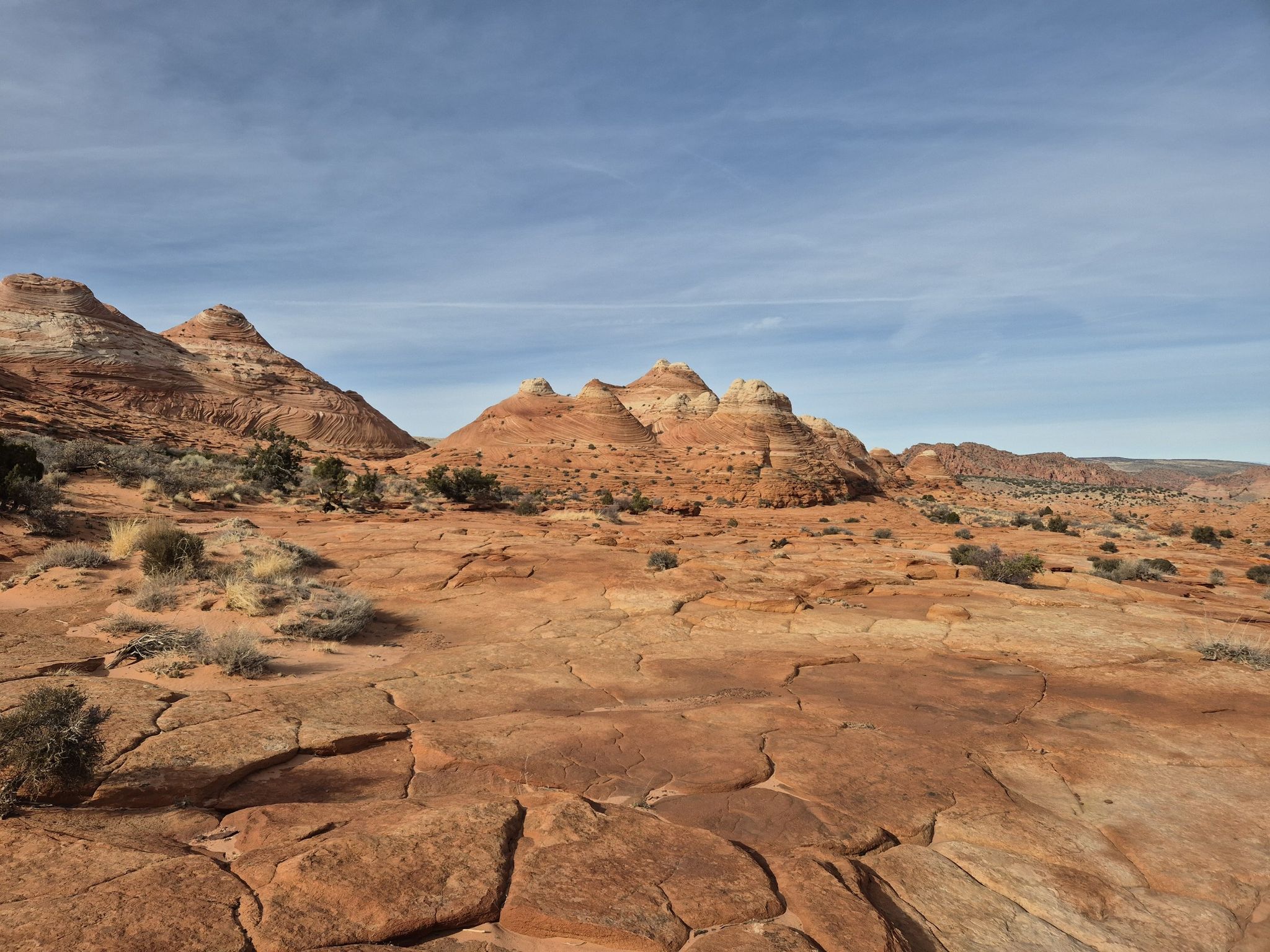 Cracked red rock ground leading to distant layered desert formations. - The Wave loop from Coyote Buttes North