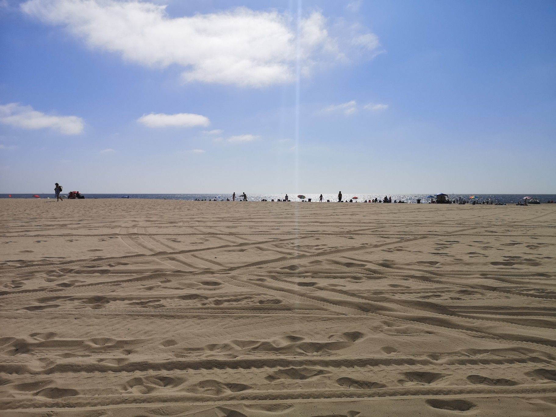 Wide sandy beach with tire tracks and many people near the ocean. - Noble Park loop from Manhattan Beach
