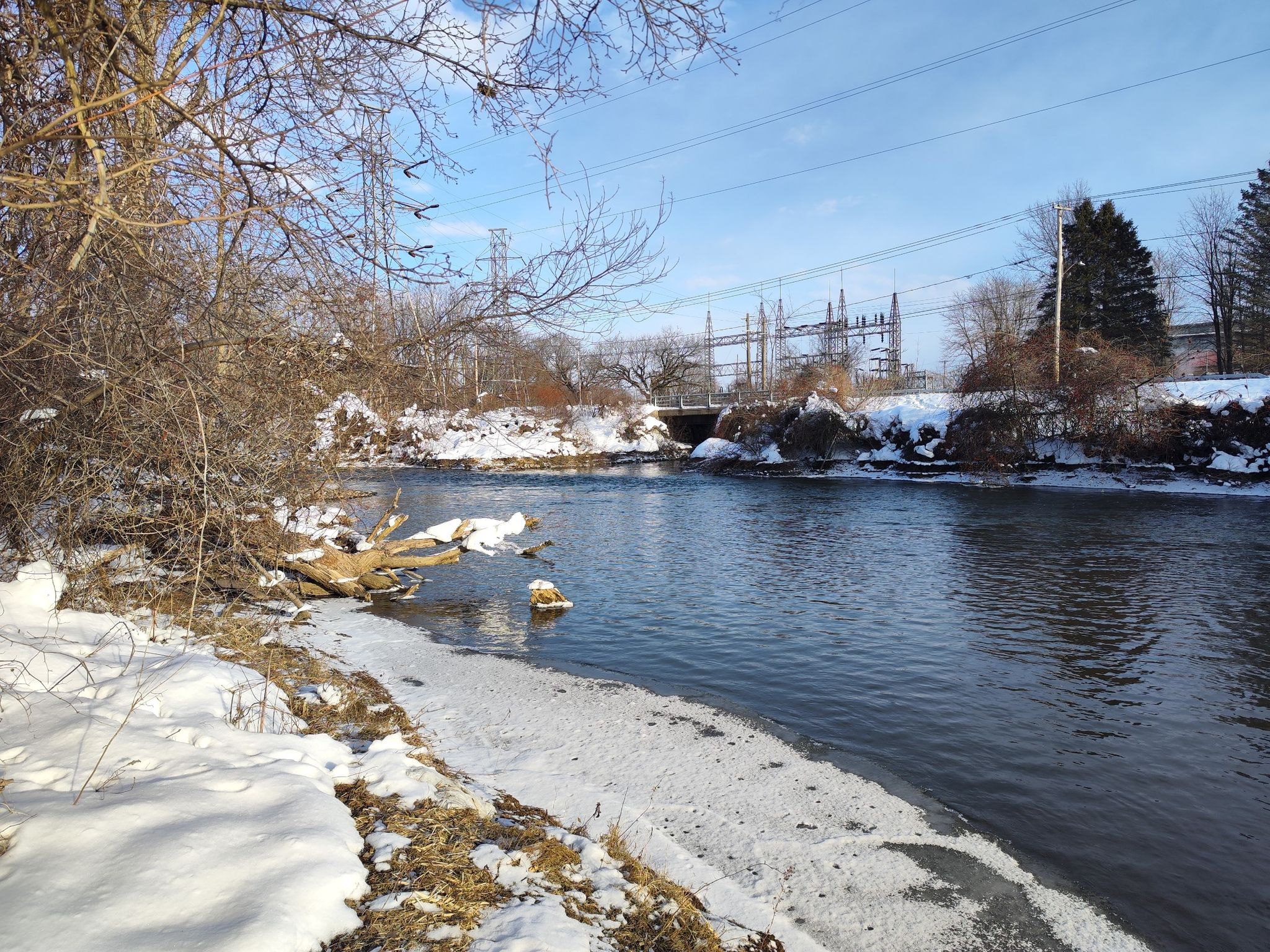 A river flows past snow-covered banks and bare trees on a bright winter day. - Mohawk River Trail – Fort Stanwix National Monument loop from City of Rome