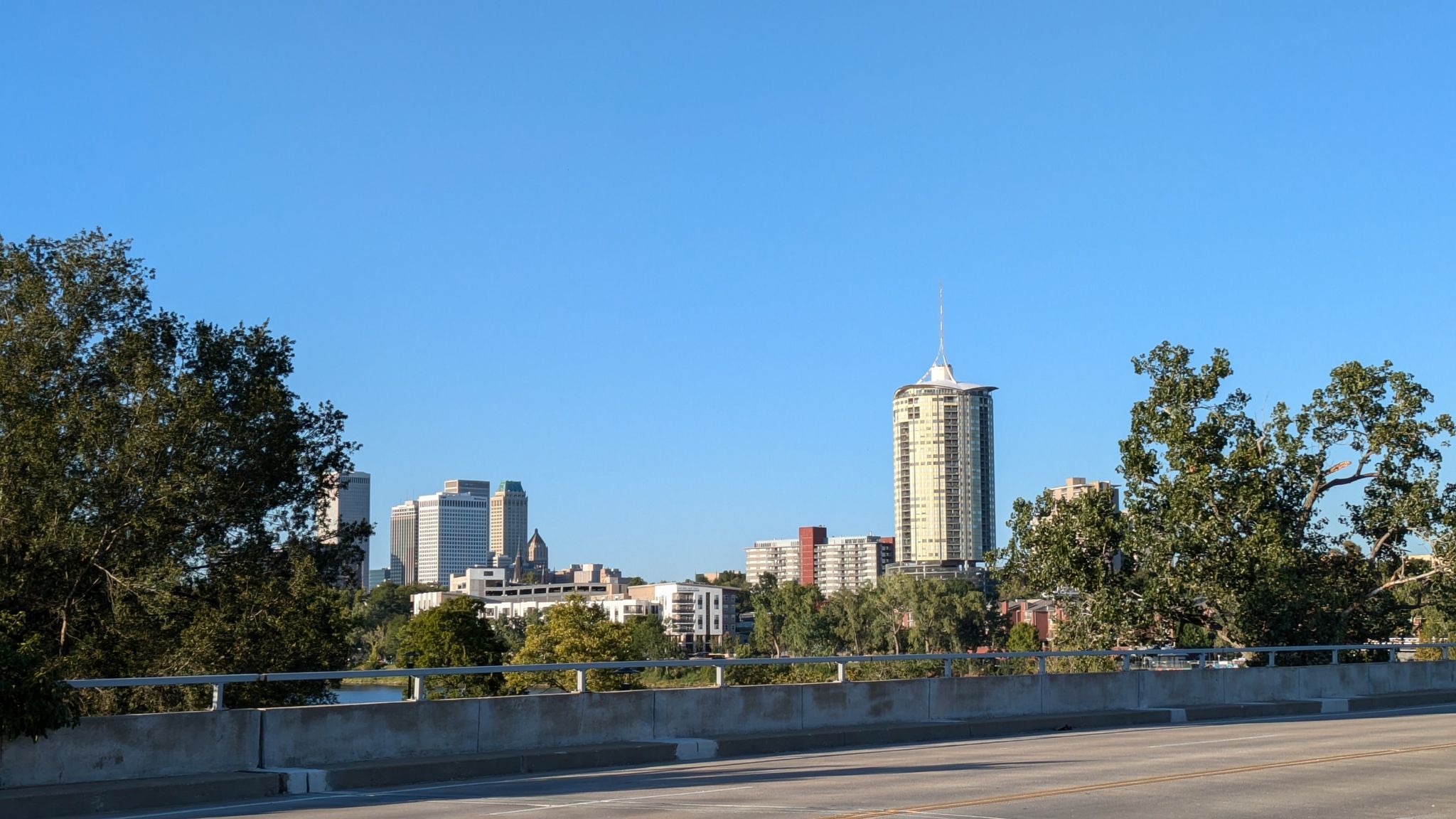 Distant city skyline with tall buildings, viewed from a bridge under a clear blue sky. - The Gathering Place – Gathering Place Park loop from Philbrook Museum of Art