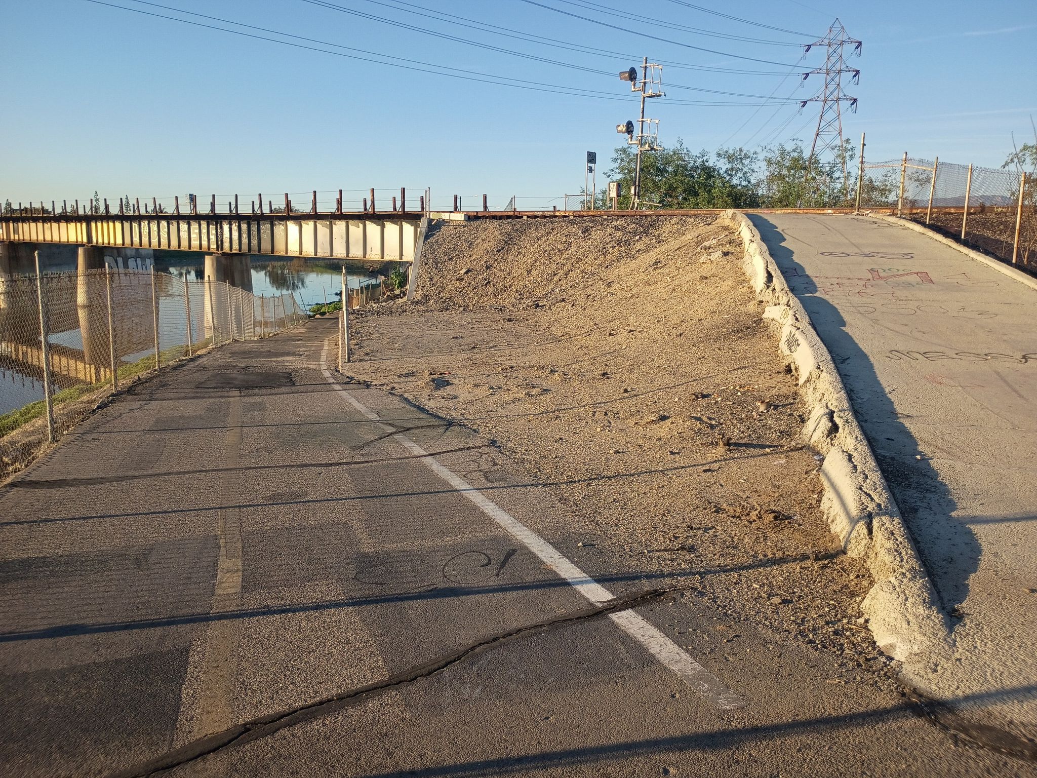 Paved path leading to a dirt ramp beside a long metal bridge. - West San Gabriel River Trail – El Dorado East Regional Park loop from West Whittier