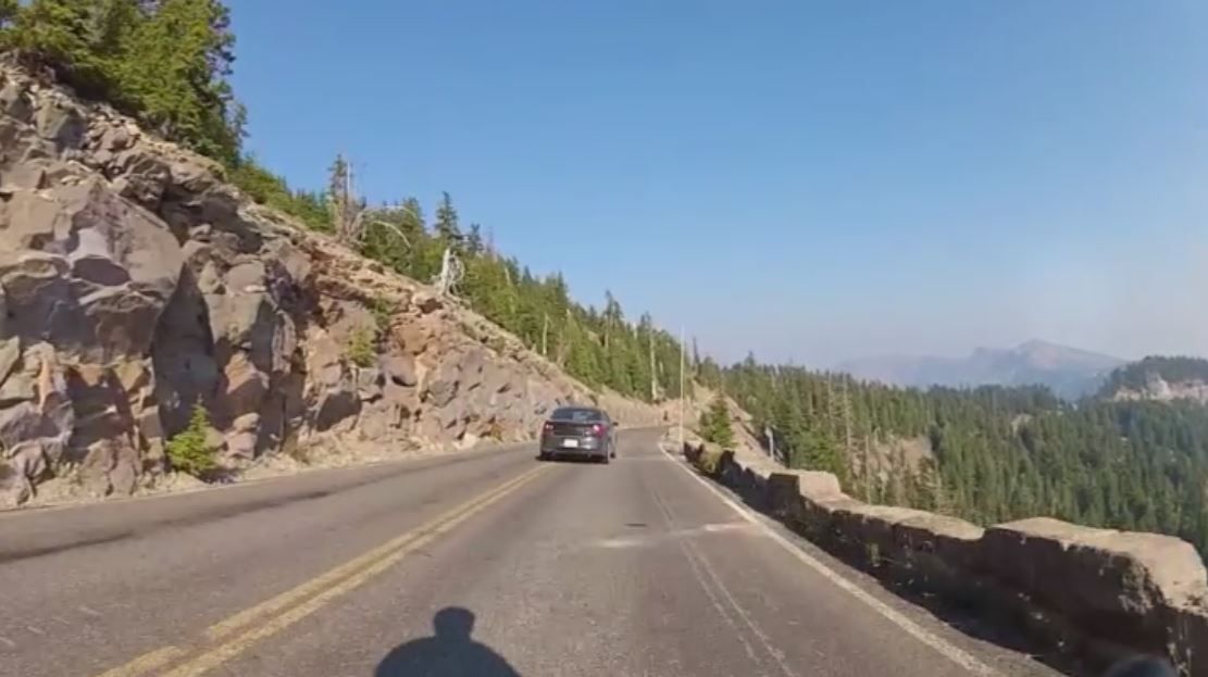 Car drives on a winding mountain road with rocky slopes and pine trees. - Dutton Creek Trail