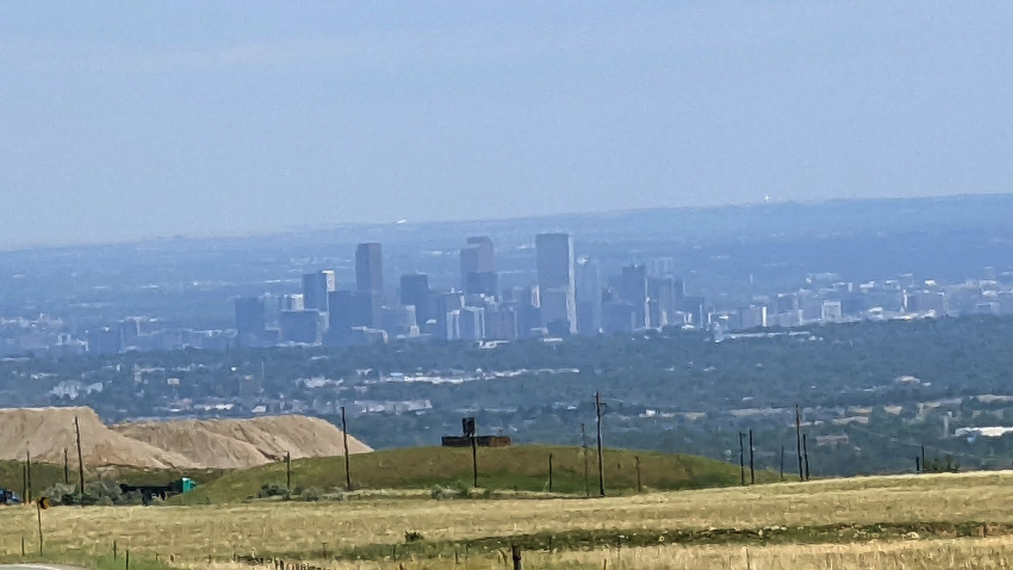 A hazy distant city skyline viewed from rolling hills and dry fields. - Colorado Tap House loop from Wheat Ridge / Ward Road