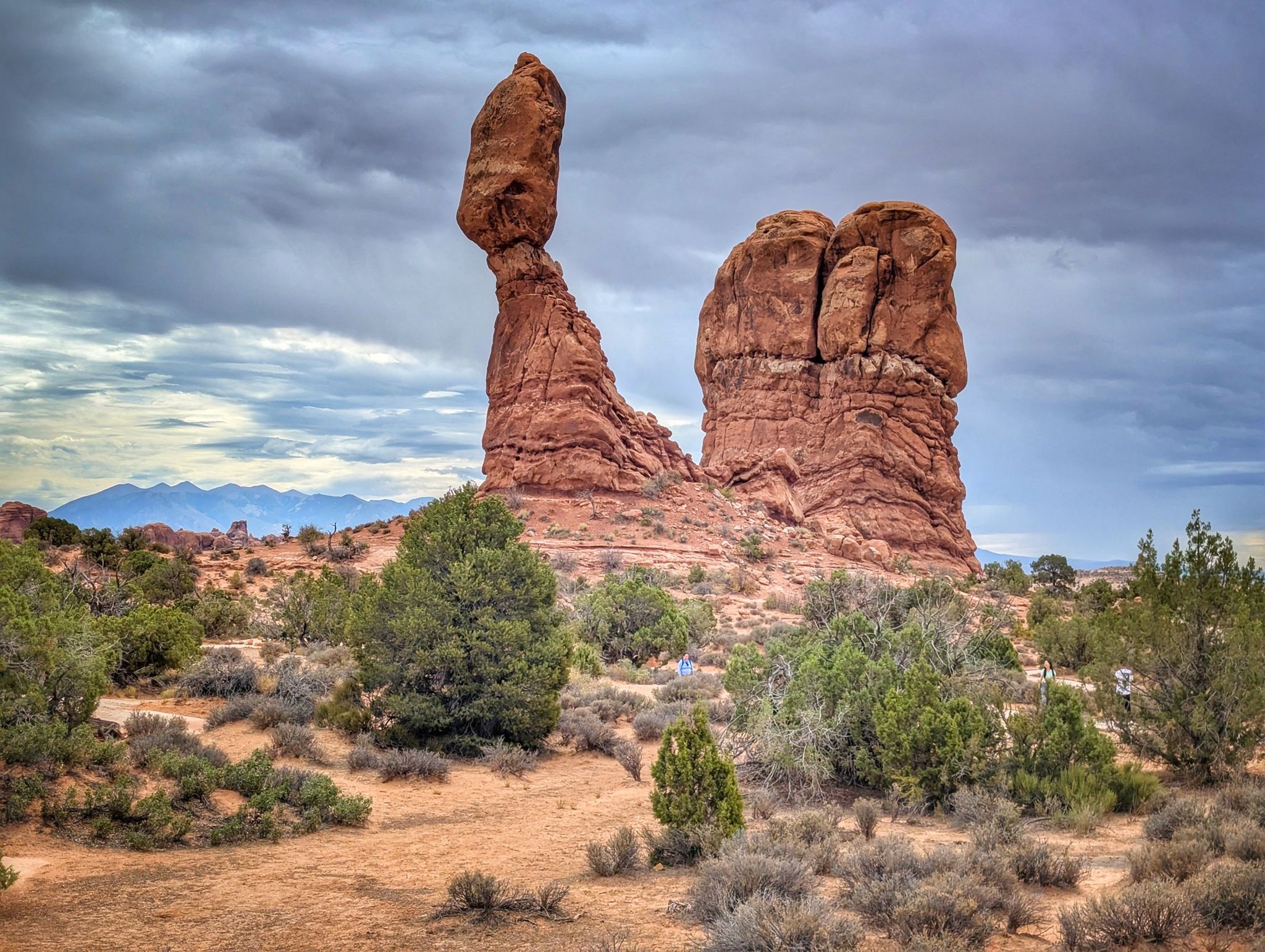 A tall, balanced red rock formation dominates a desert landscape under cloudy skies. - Willow Springs Road