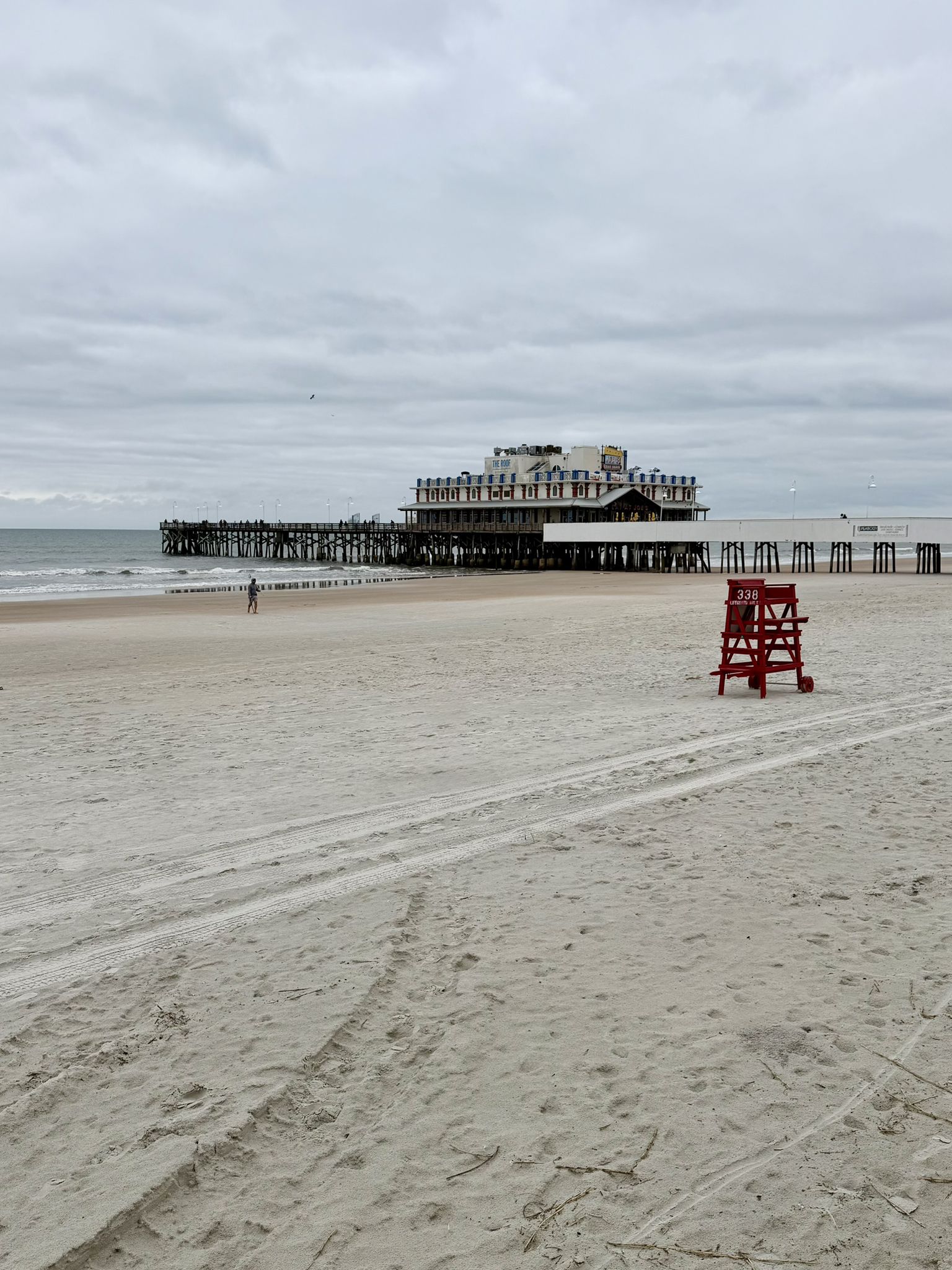 Overcast beach with a red lifeguard chair and a long pier. - Daytona Beach Boardwalk