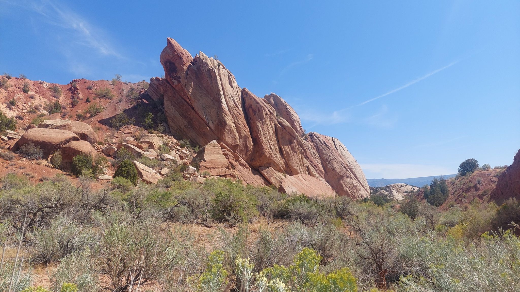 Large, jagged red rock formation dominates a desert landscape under a clear blue sky. - Sound of Silence Trail – Dinosaur National Monument