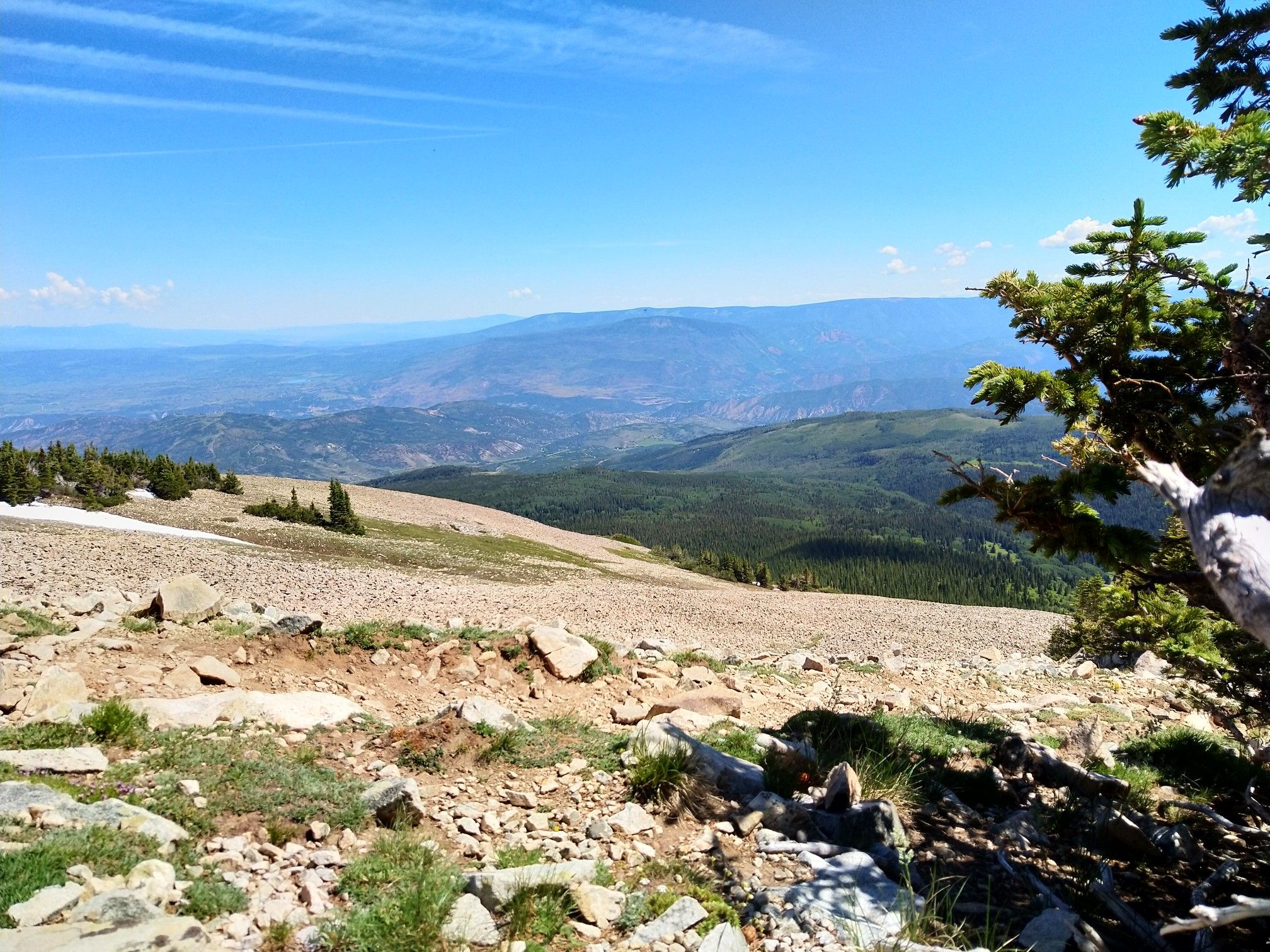 Rocky mountain slope with sparse vegetation, snow patches, and distant green hills. - Mount Sopris Trail
