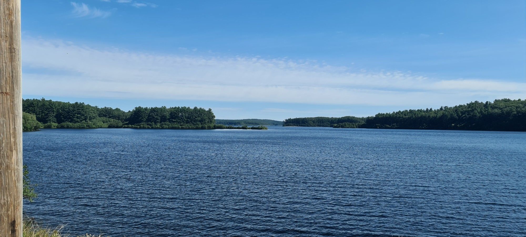 Expansive blue lake surrounded by green forests under a bright, clear sky. - Wachusett Reservoir Watershed loop from Worcester