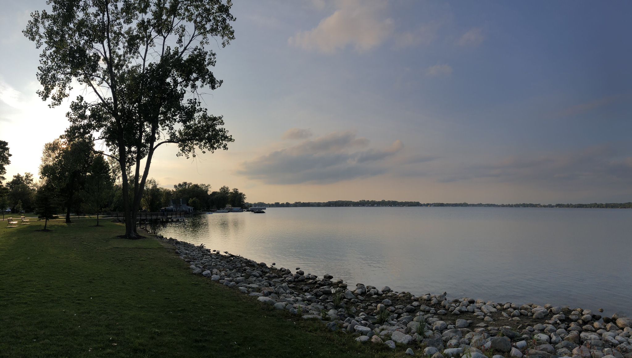 A calm lake at sunset, with a rocky shore and trees on the left. - Walled Lake loop