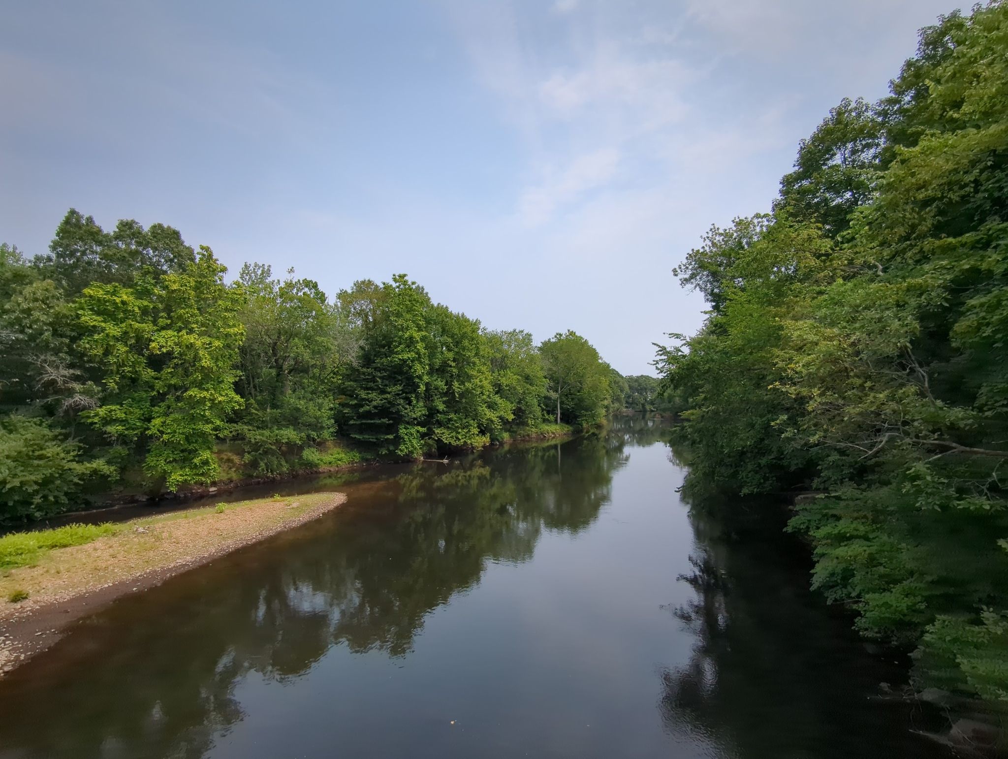 A calm river reflects green trees and a light blue sky. - Blackstone River Bikeway – Blackstone River Bikeway loop from Providence