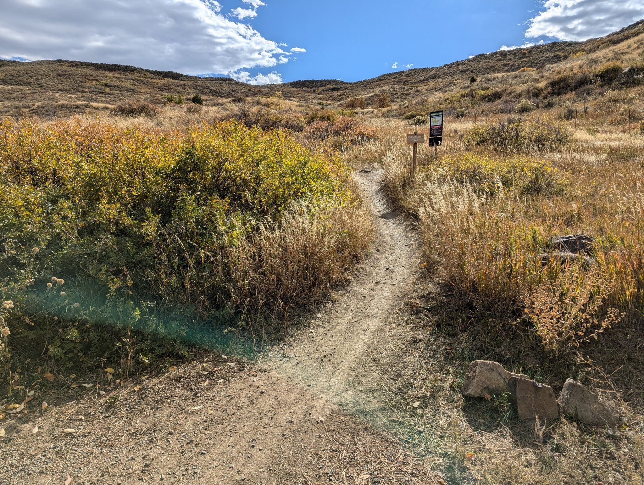 A winding dirt path leads through dry, grassy hills under a sunny sky. - Basalt Cap Loop Trail