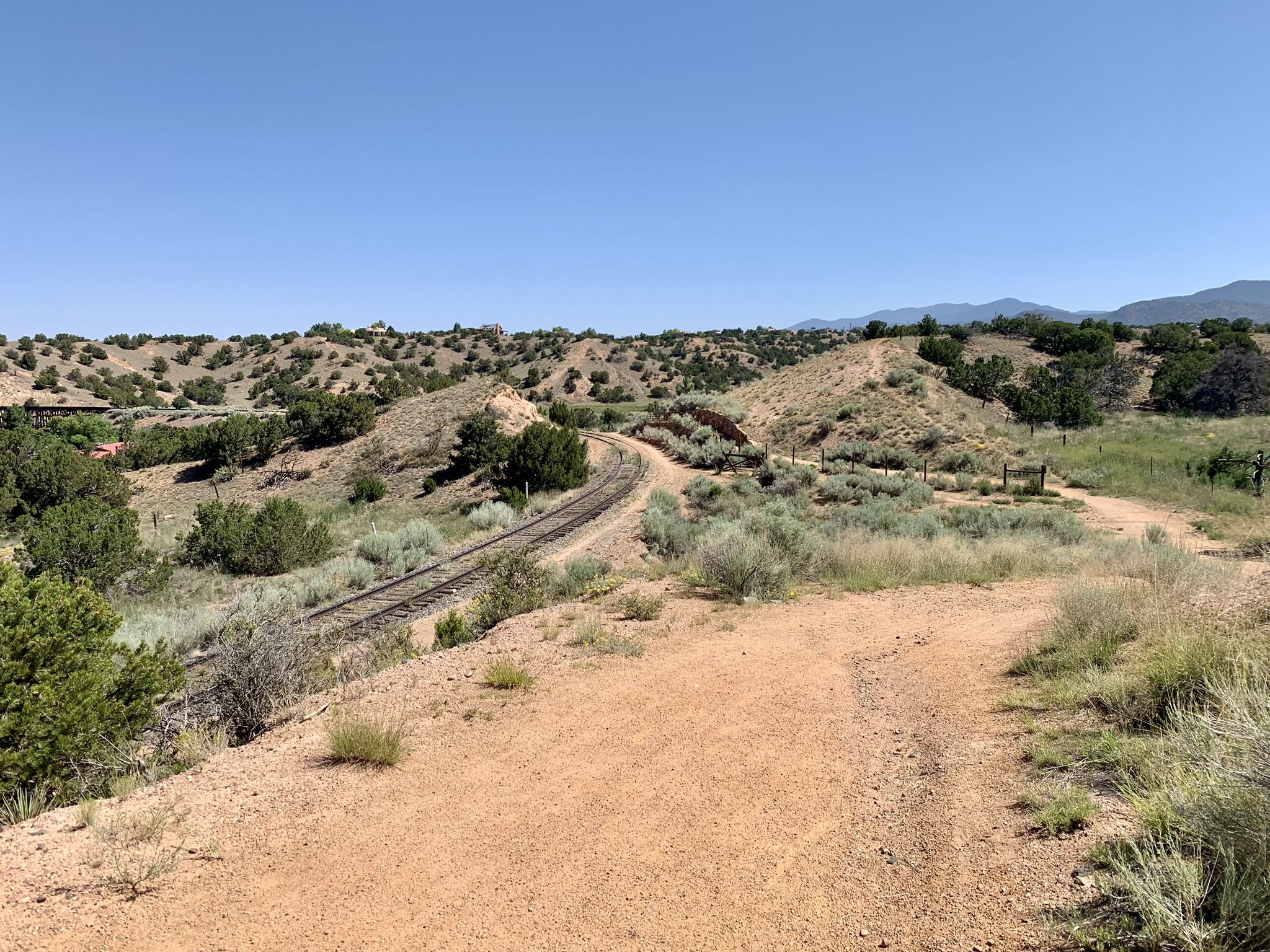 A dirt path overlooks train tracks winding through arid, brush-covered hills. - Running loop from Rail Trail Parking