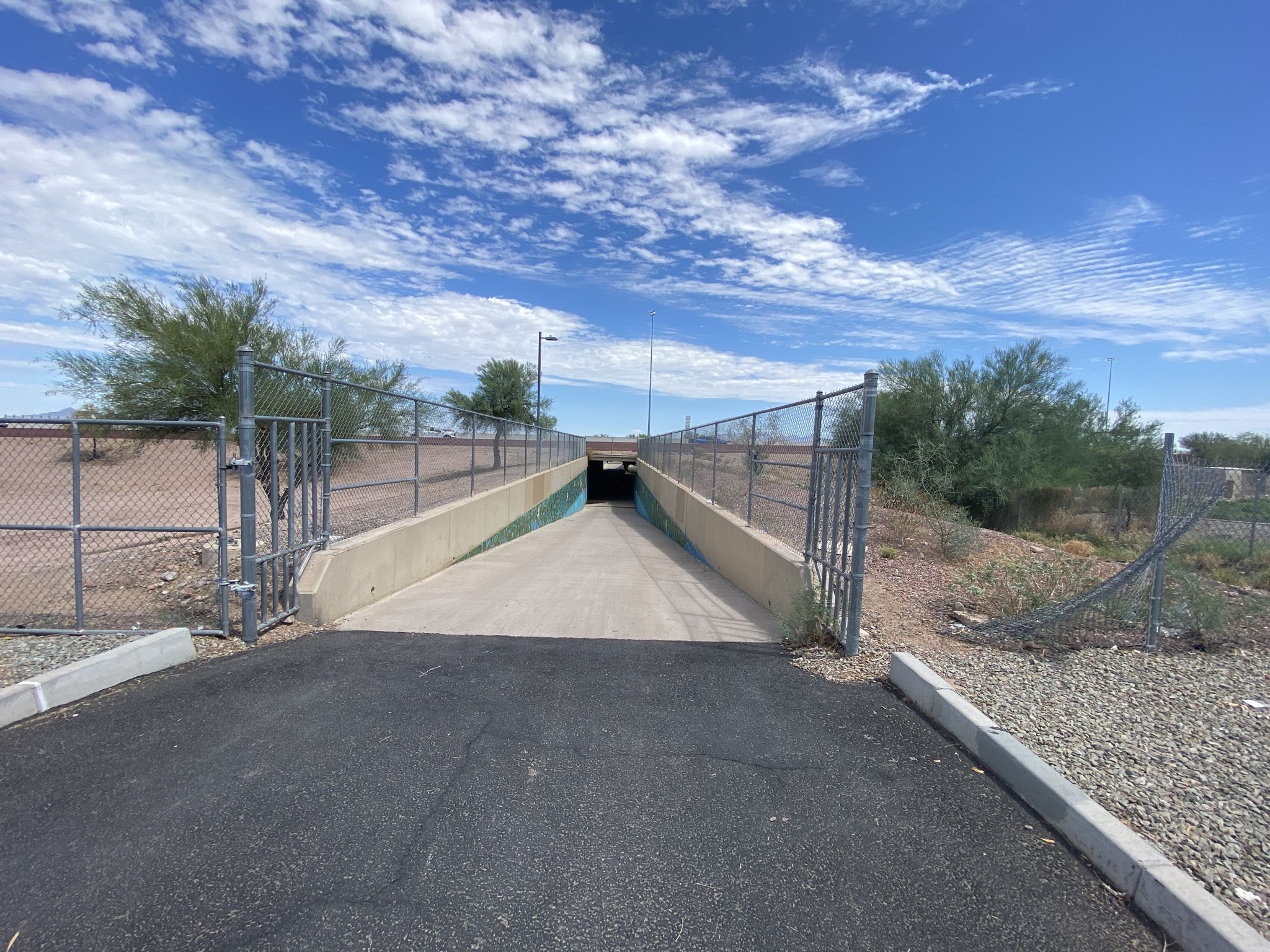 Sunny view of a concrete underpass entrance with chain-link fences and dry brush. - Rio Salado Pathway
