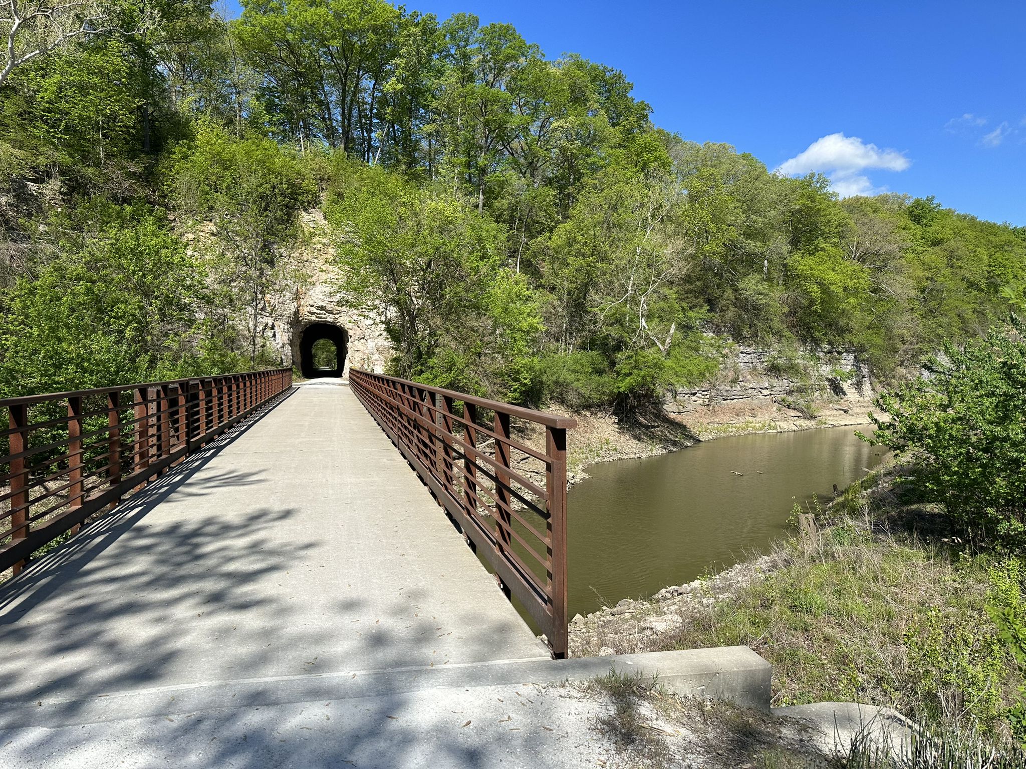 A bridge leads to a tunnel entrance, with a river and green trees. - Katy Trail: Boonville to Rocheport