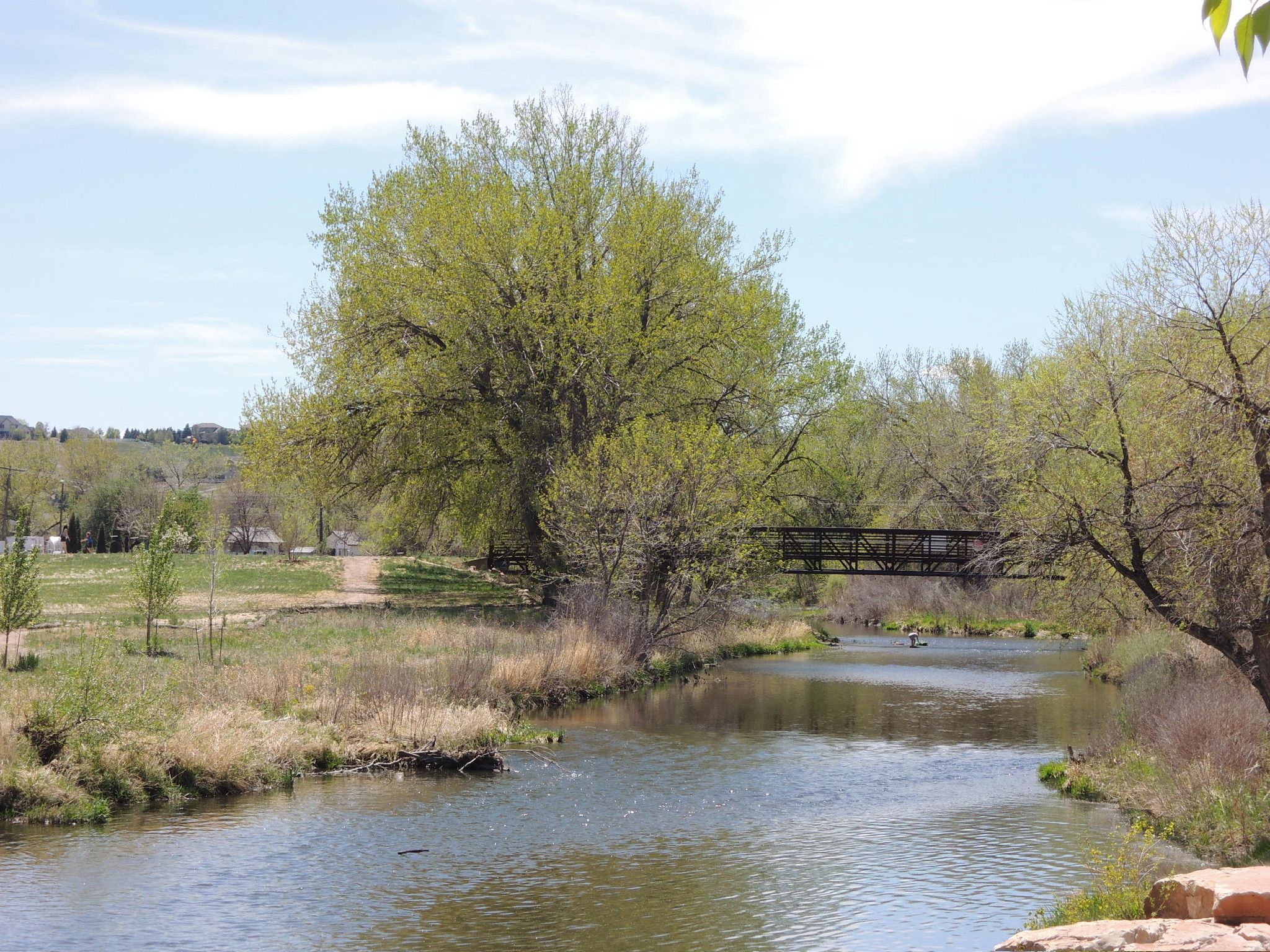 A river flows past green trees and a dark bridge under a bright sky. - Windsor Lake Loop Trail