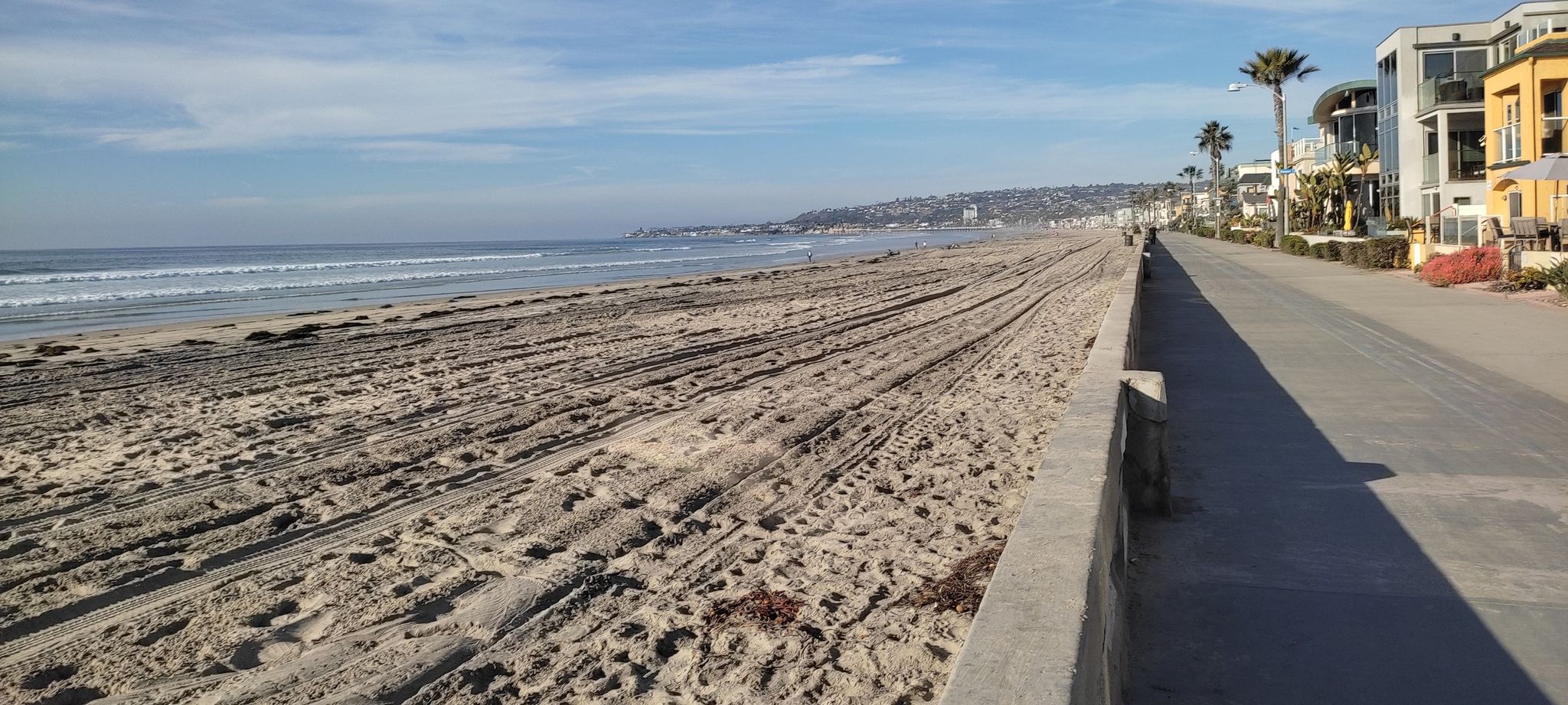 A wide sandy beach with ocean waves, a boardwalk, and coastal houses. - Ocean Front Walk