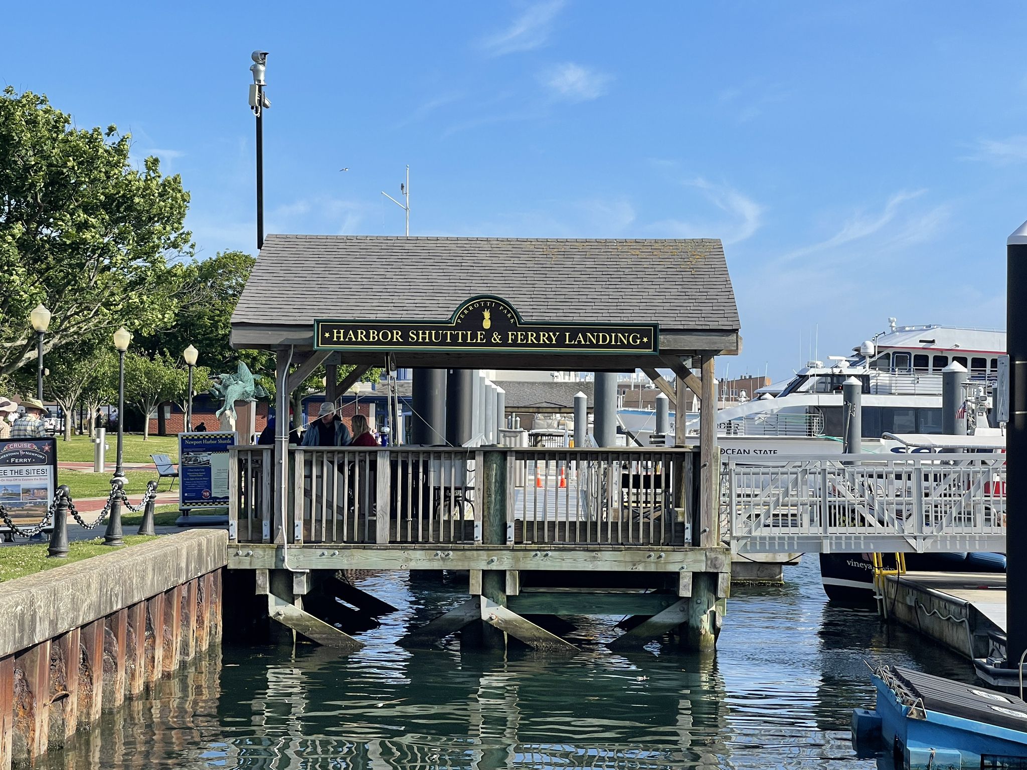 Sunny ferry landing structure over water with boats and people waiting. - Washington Square – Fort Adams State Park loop from Newport