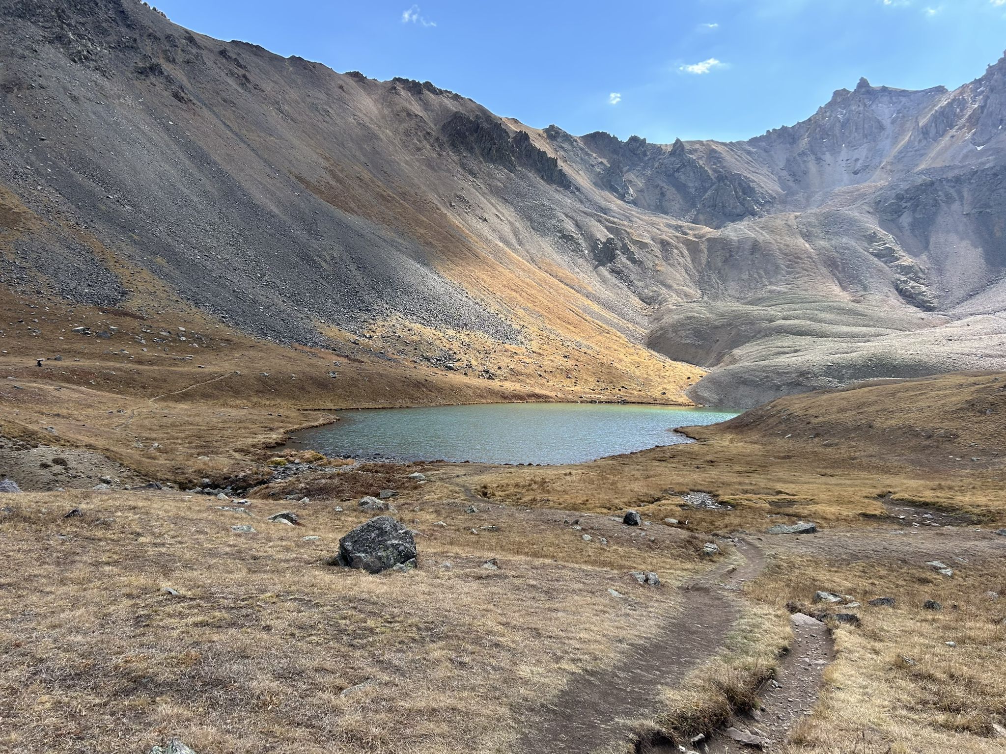 Serene mountain lake surrounded by vast, rocky, and dry slopes under a bright sky. - Blue Lakes Trail