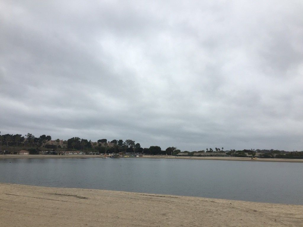 Calm water and sandy shore under a wide, overcast sky. - Newport Dunes Loop