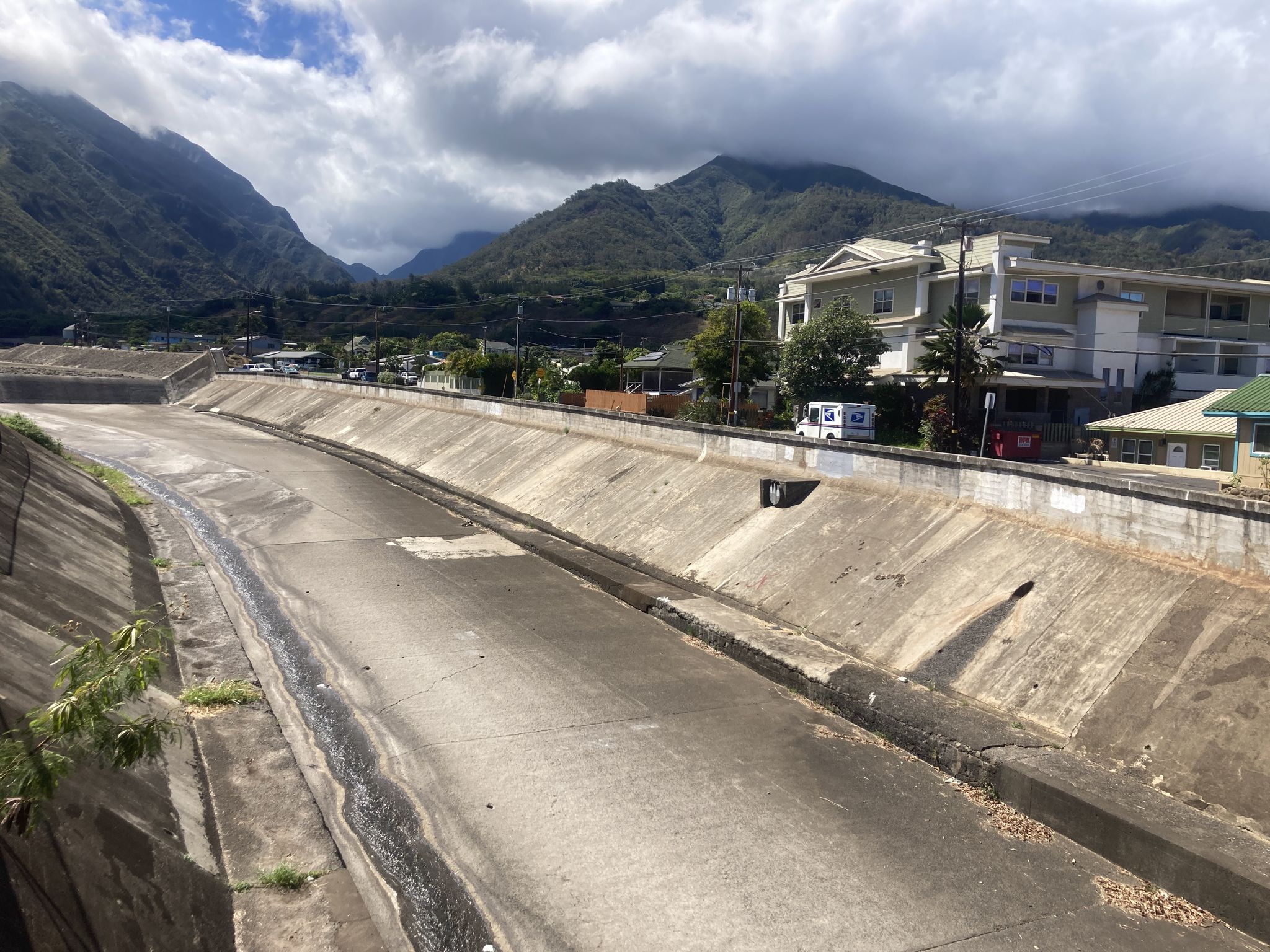 Concrete flood channel with mountains and buildings under cloudy skies. - Wai‘ehu Beach via Wailuku lopo