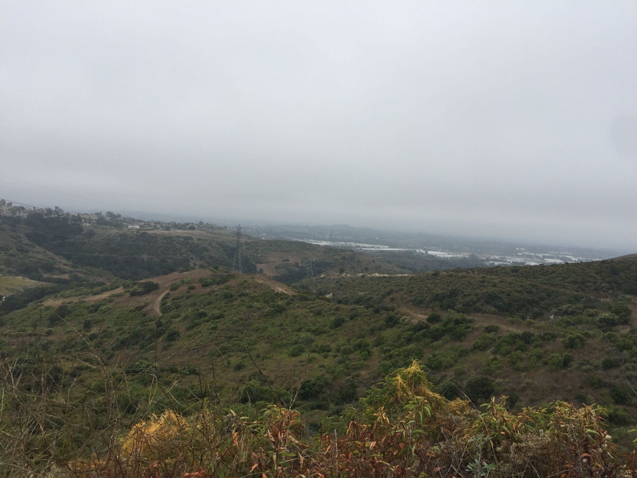 Overcast view of green hills overlooking a hazy distant urban area. - Whiting Ranch Wilderness Park – Reynolds Bench loop from Saddleback Church