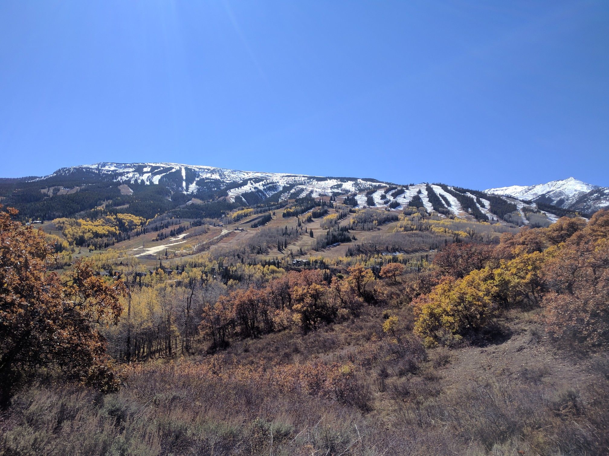 Snow-covered mountain with ski runs overlooks vibrant autumn trees under a clear sky. - Rim Trail South to Spiral Point