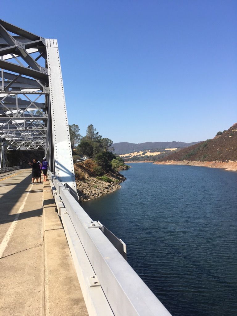 Two people walk on a metal bridge over a wide blue river. - Sutter's Mill – Folsom Lake loop from Oak Avenue Whistlestop