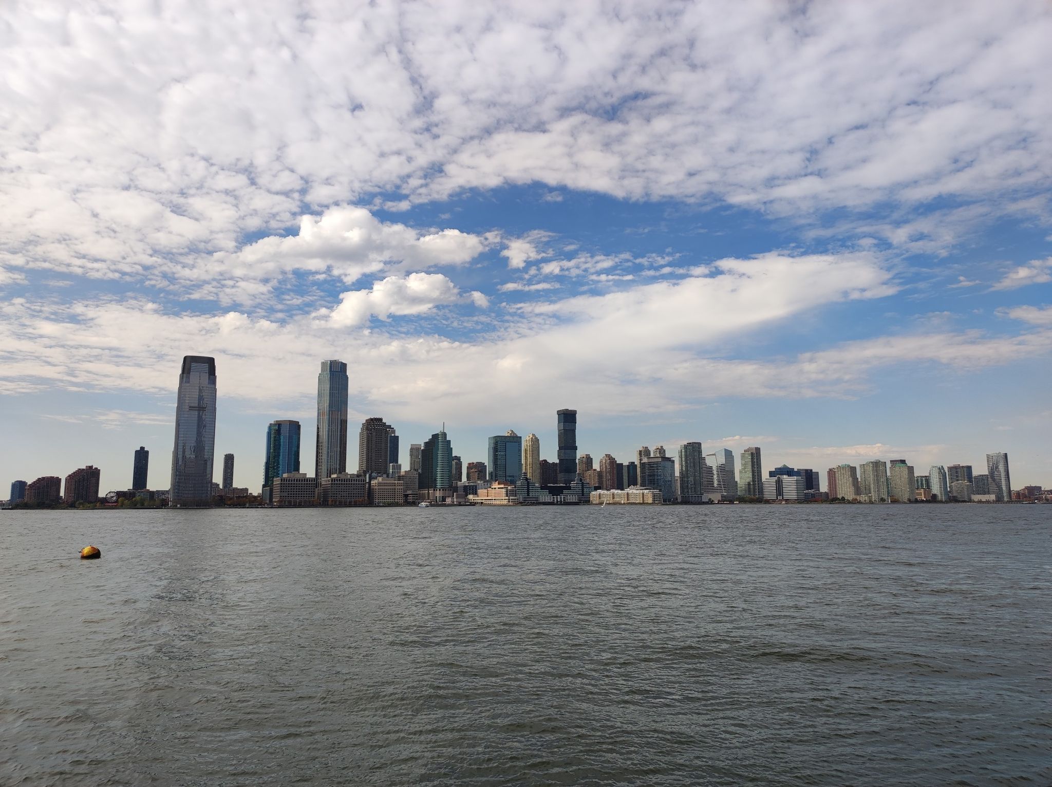 City skyline across water under a blue sky with scattered white clouds. - North Cove Marina – Brookfield Place loop from New York
