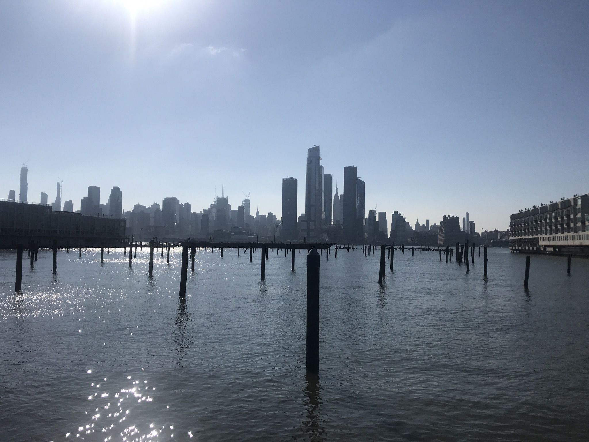 Sunny river view with many pilings, silhouetted city skyline in bright light. - Bike loop from 2nd Street