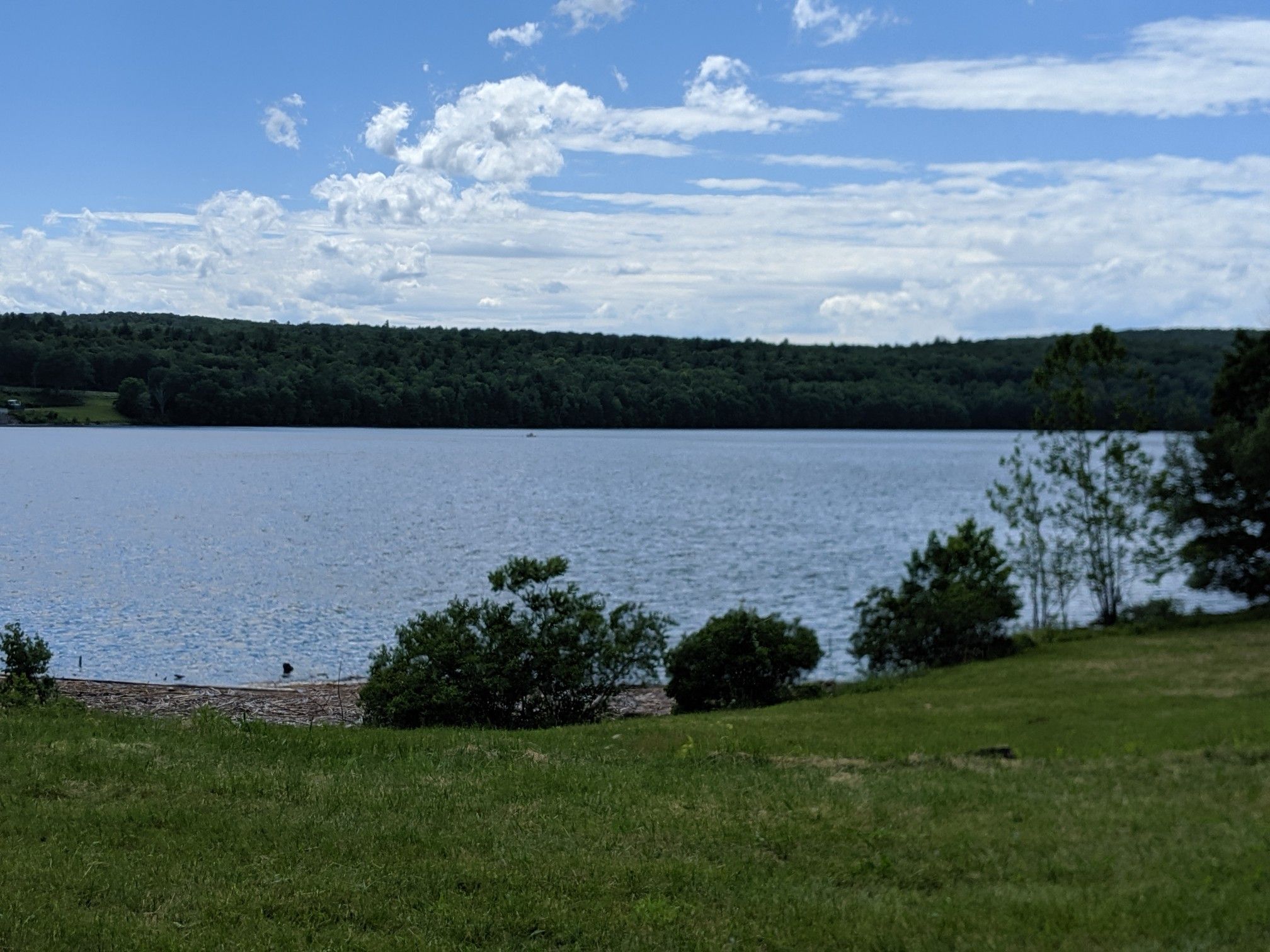 Expansive lake with a distant forested shoreline under a bright, cloudy sky. - Peekamoose Lake – Peekamoose Blue Hole loop from Accord