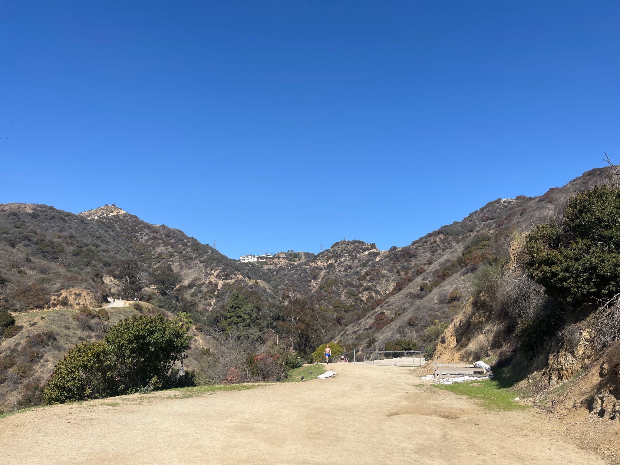A wide dirt path leads into a valley between two brush-covered hillsides. - Runyon Canyon Vista Entrance – Inspiration Point loop from West Hollywood