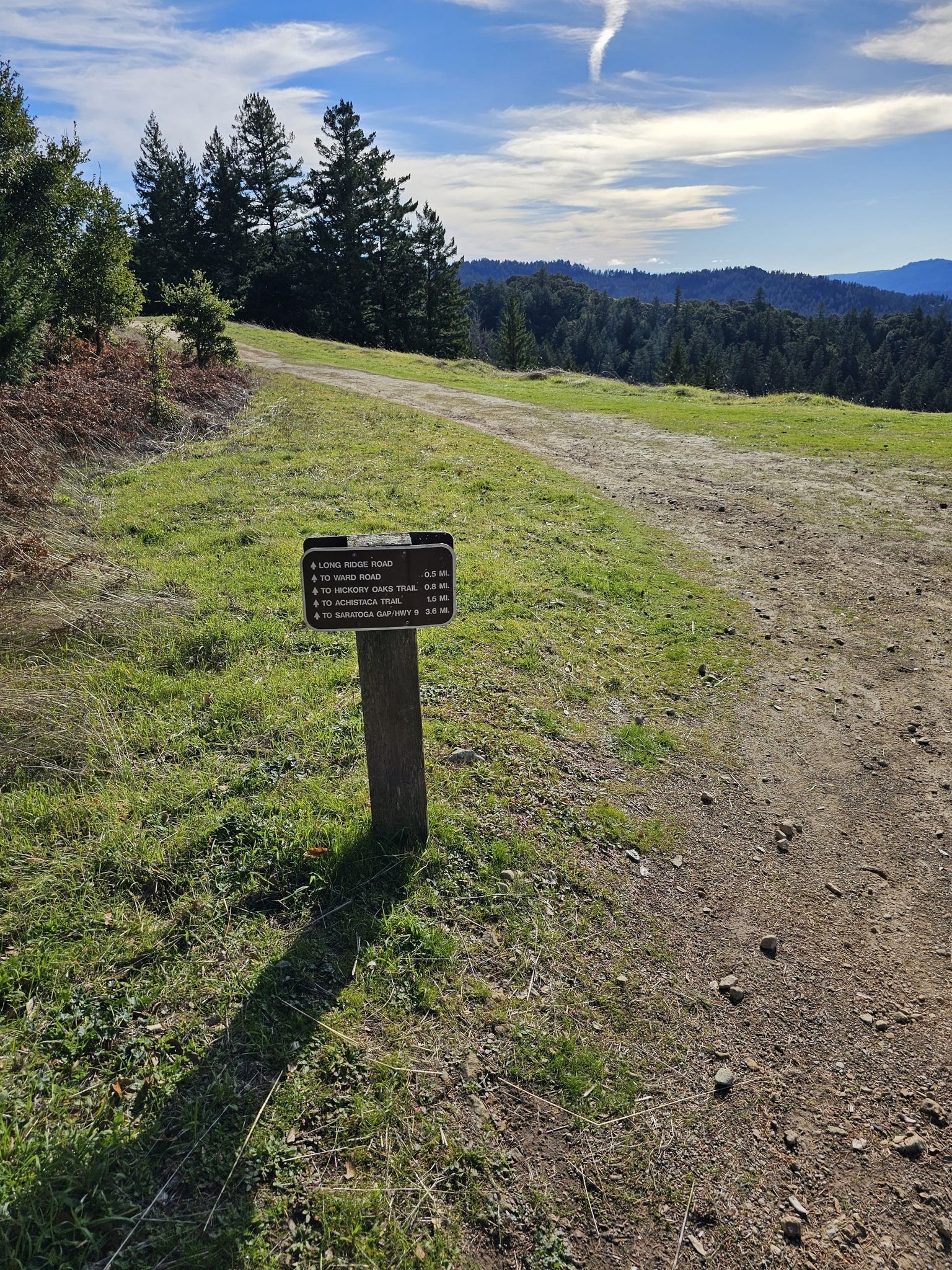 Trail signpost on a dirt path overlooking forested hills under a cloudy sky. - Long Ridge Loop
