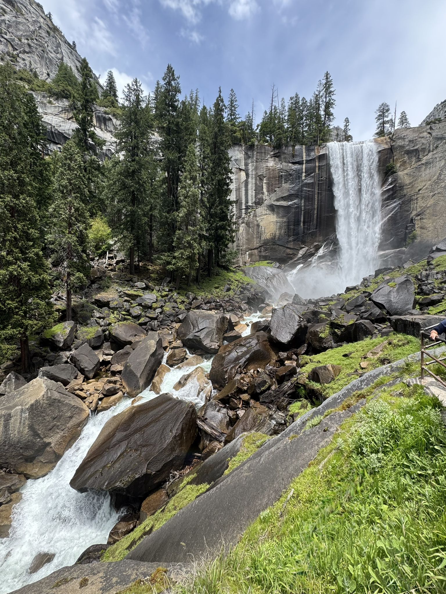 A large waterfall cascades into a rocky river, with a person on a path. - Mist Trail to Vernal Fall