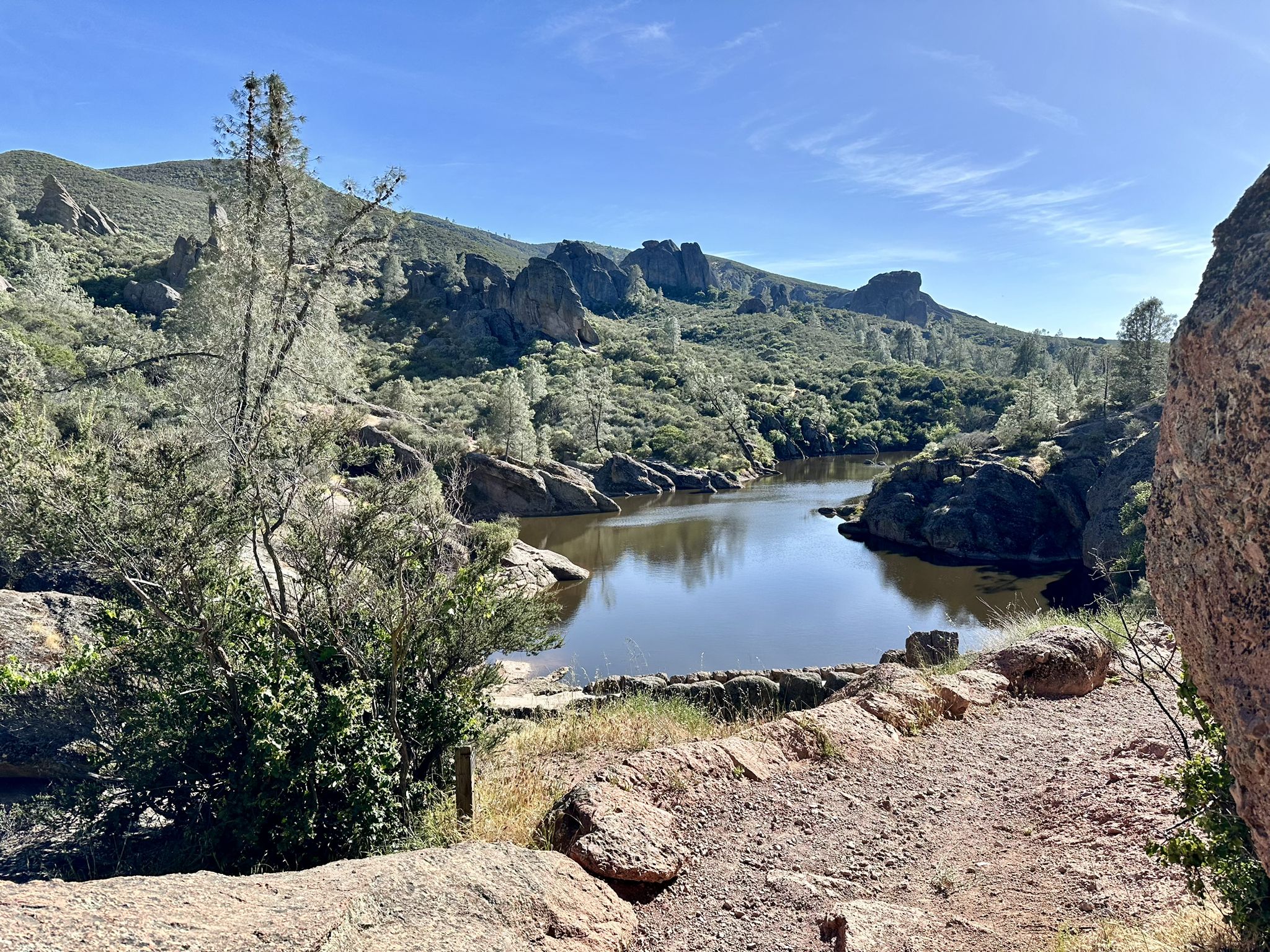 Calm lake surrounded by rocky hills and green trees under bright blue sky. - Moses Spring and Rim Trail Loop