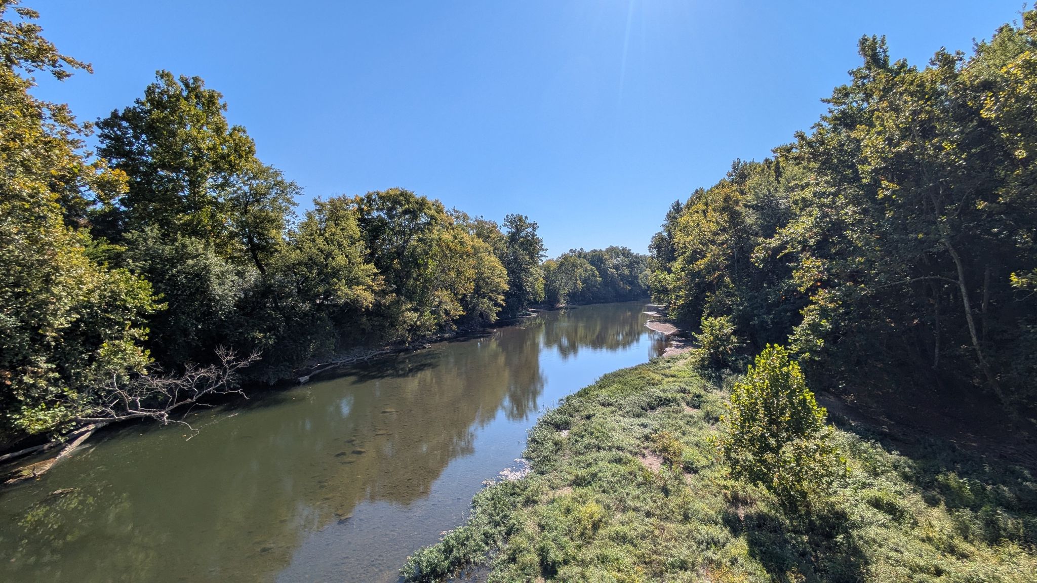 A wide river flowing between lush green trees under a clear blue sky. - Monon and Fall Creek Trail Loop