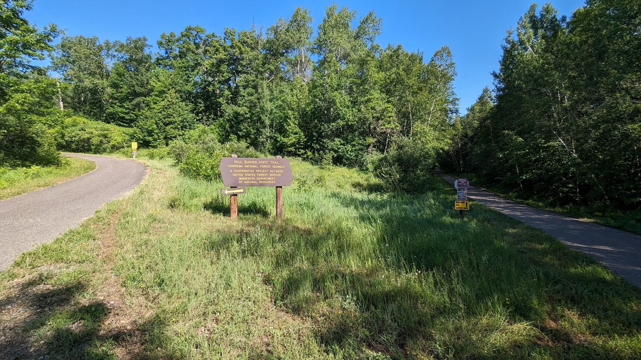 Information sign on a grassy area next to a paved path, surrounded by trees. - Shingobee Junction loop from Hackensack
