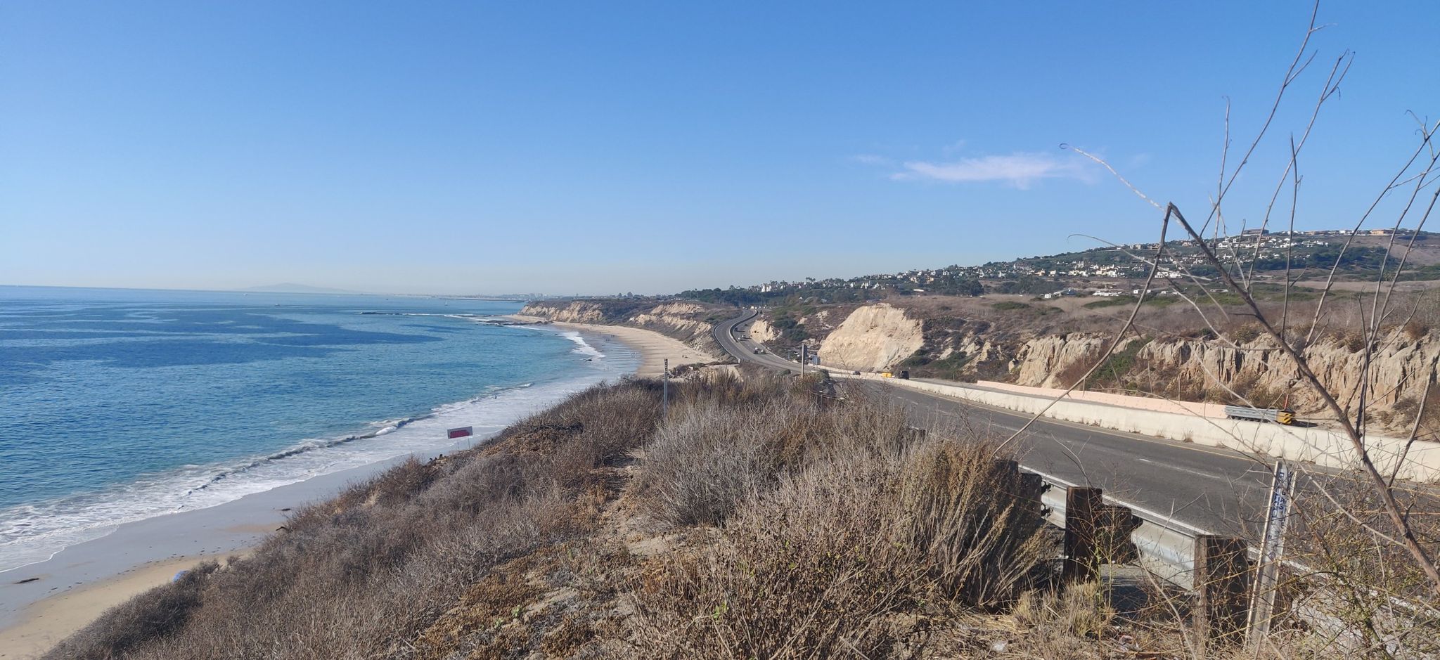 Panoramic coastal view with blue ocean, sandy beach, cliffs, and a road. - San Juan Capistrano to Newport Bay via Crystal Cove State Park