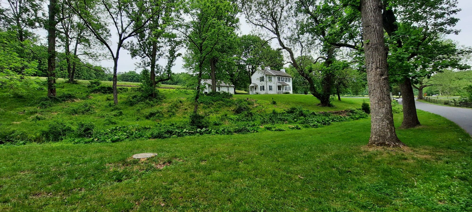 White house on a grassy hill, surrounded by trees under an overcast sky. - Schuylkill River loop from Pottstown