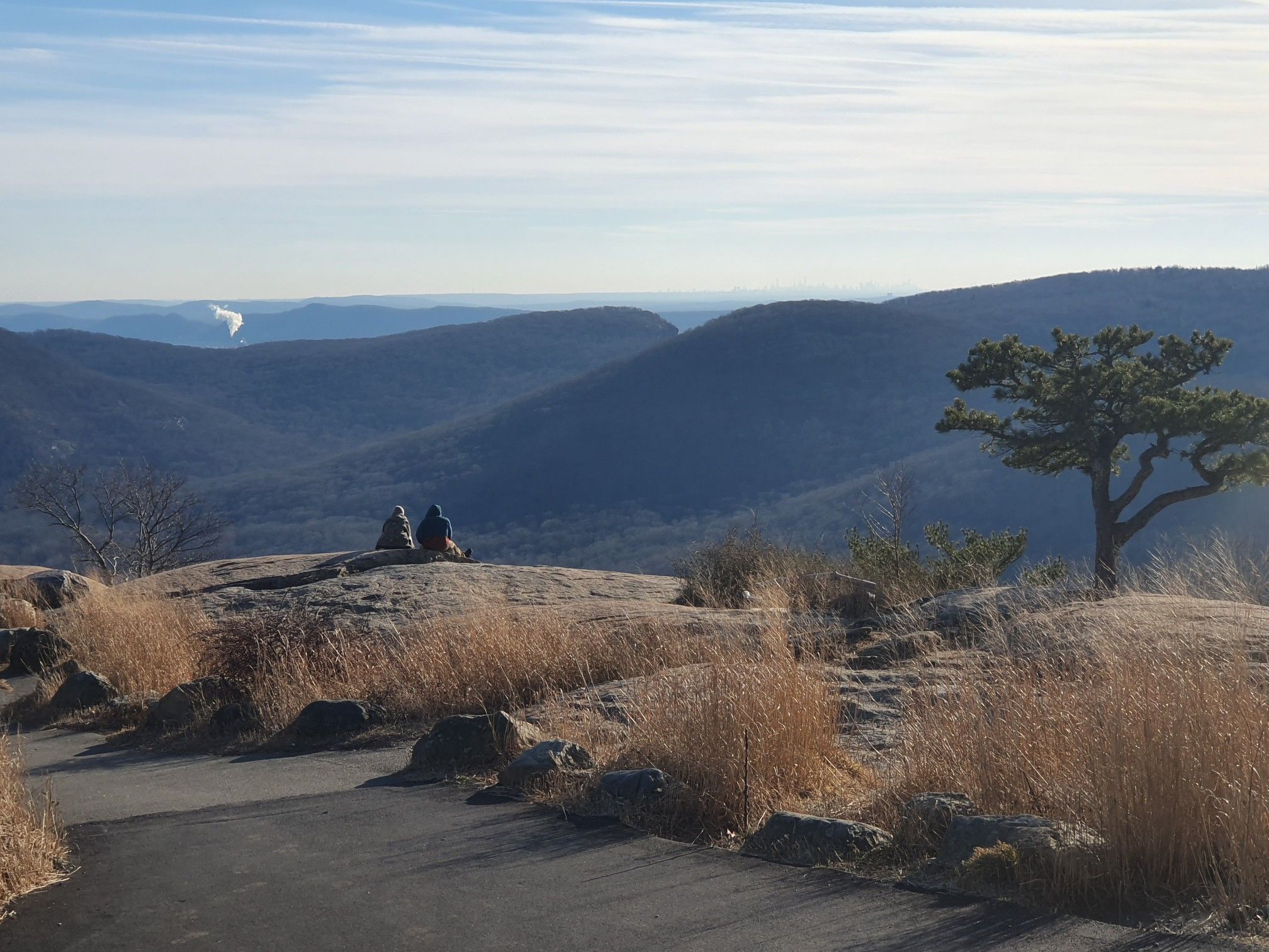 Two people sit on rocks, overlooking vast blue mountains under a clear sky. - Bear Mountain Climb – View from Bear Mountain Summit loop from Anthony's Nose