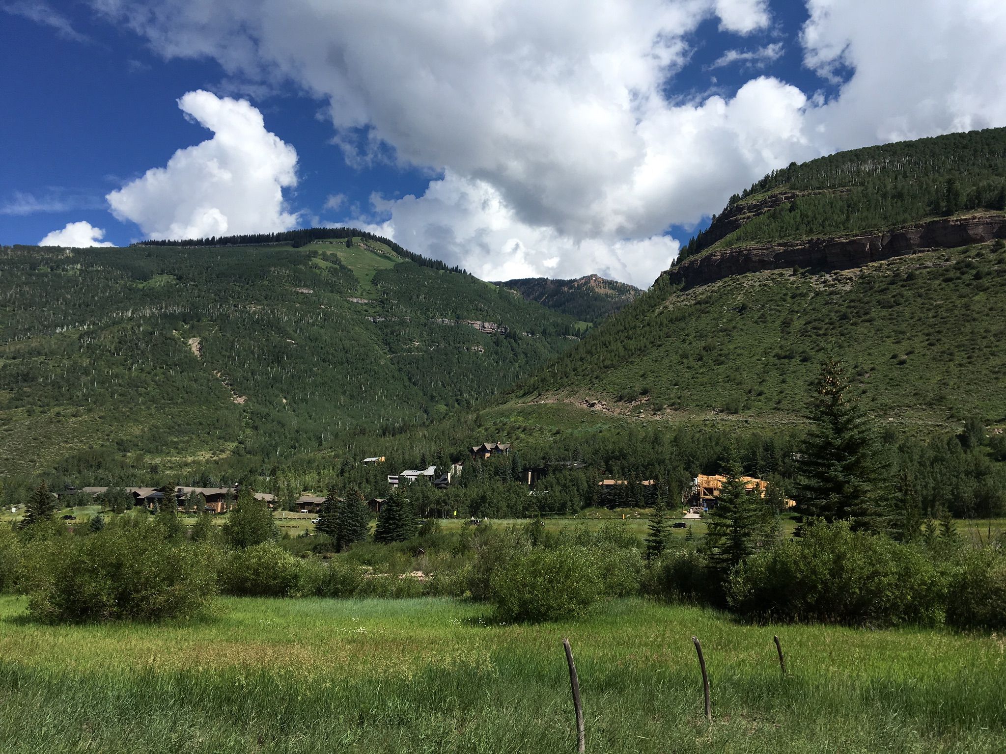 Green mountains under a cloudy sky, with distant buildings and trees. - Minturn, Red Cliff, and Vail Pass loop from Vail