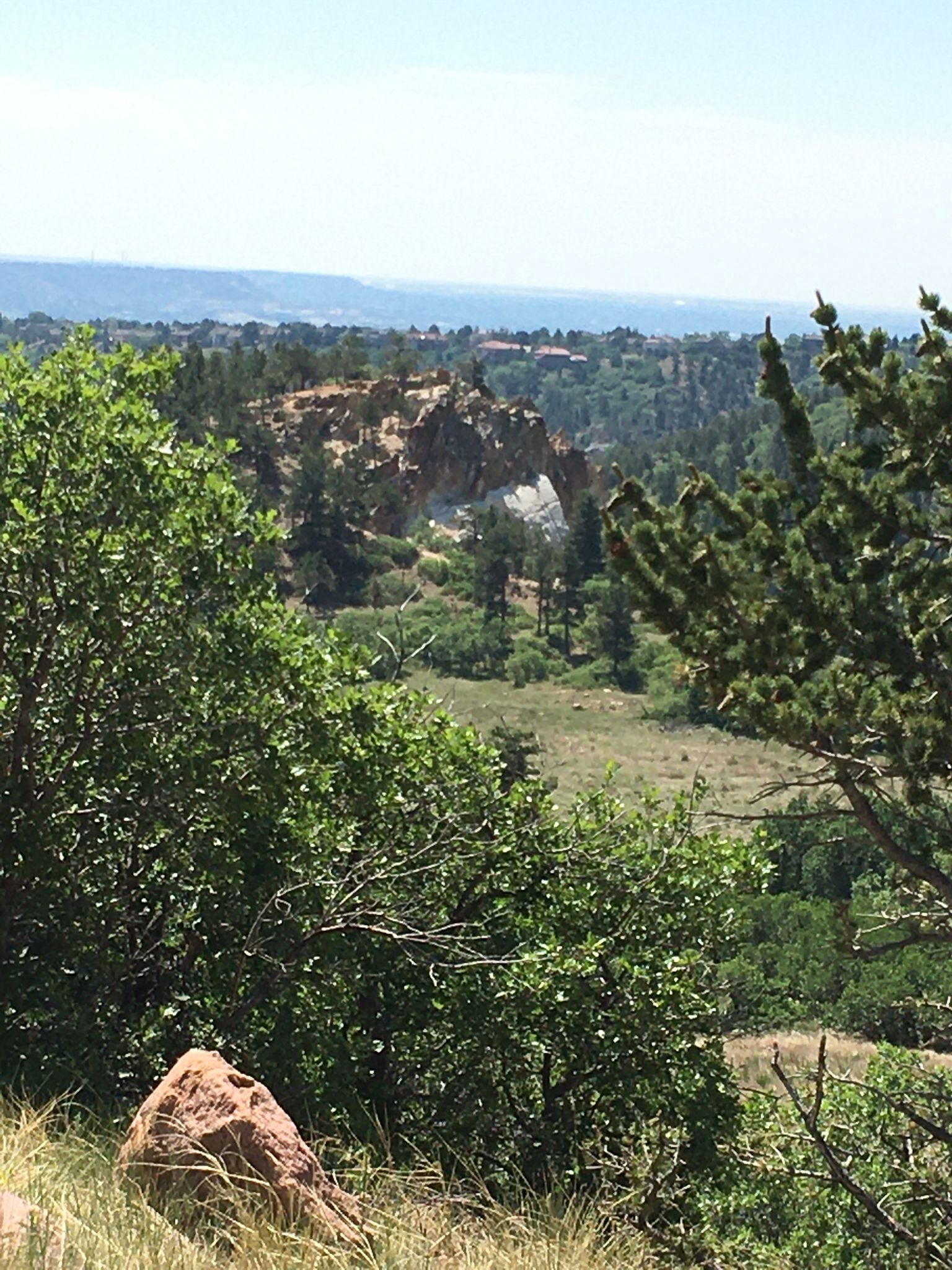 Distant rock formation and valley seen through lush green trees. - View of Blodgett Peak – Falcon Trail loop from Blodgett Peak Open Space