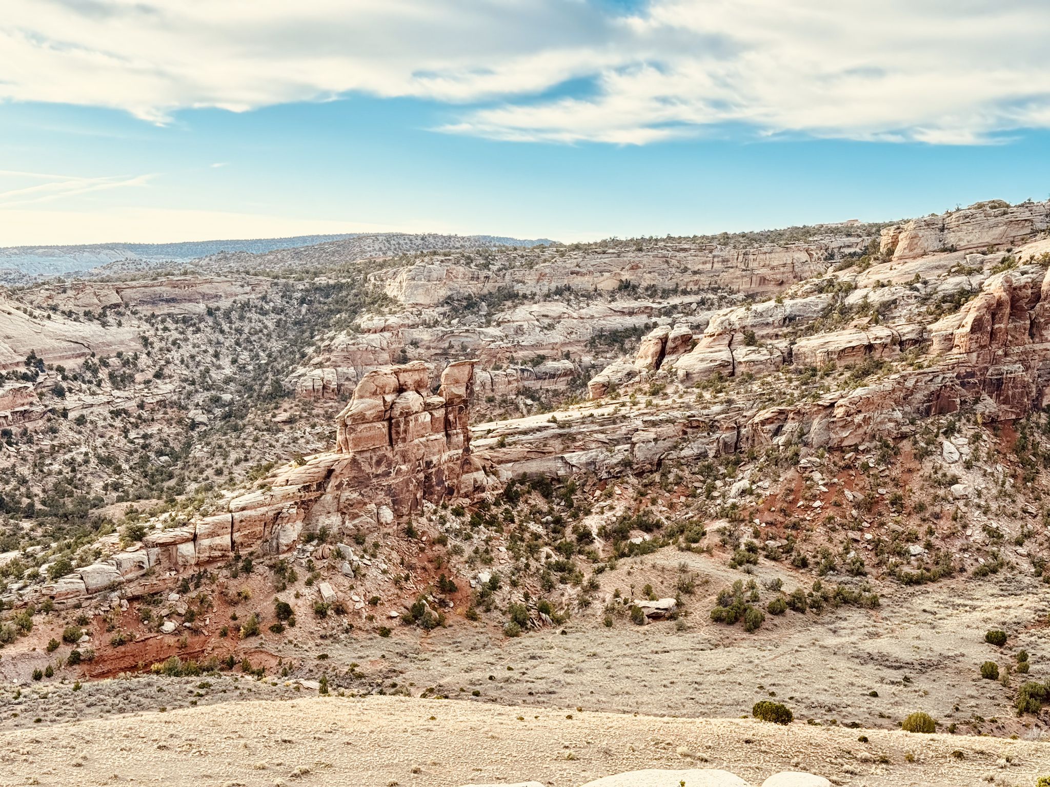 Expansive desert landscape with layered sandstone formations under a partly cloudy sky. - Serpents Trail