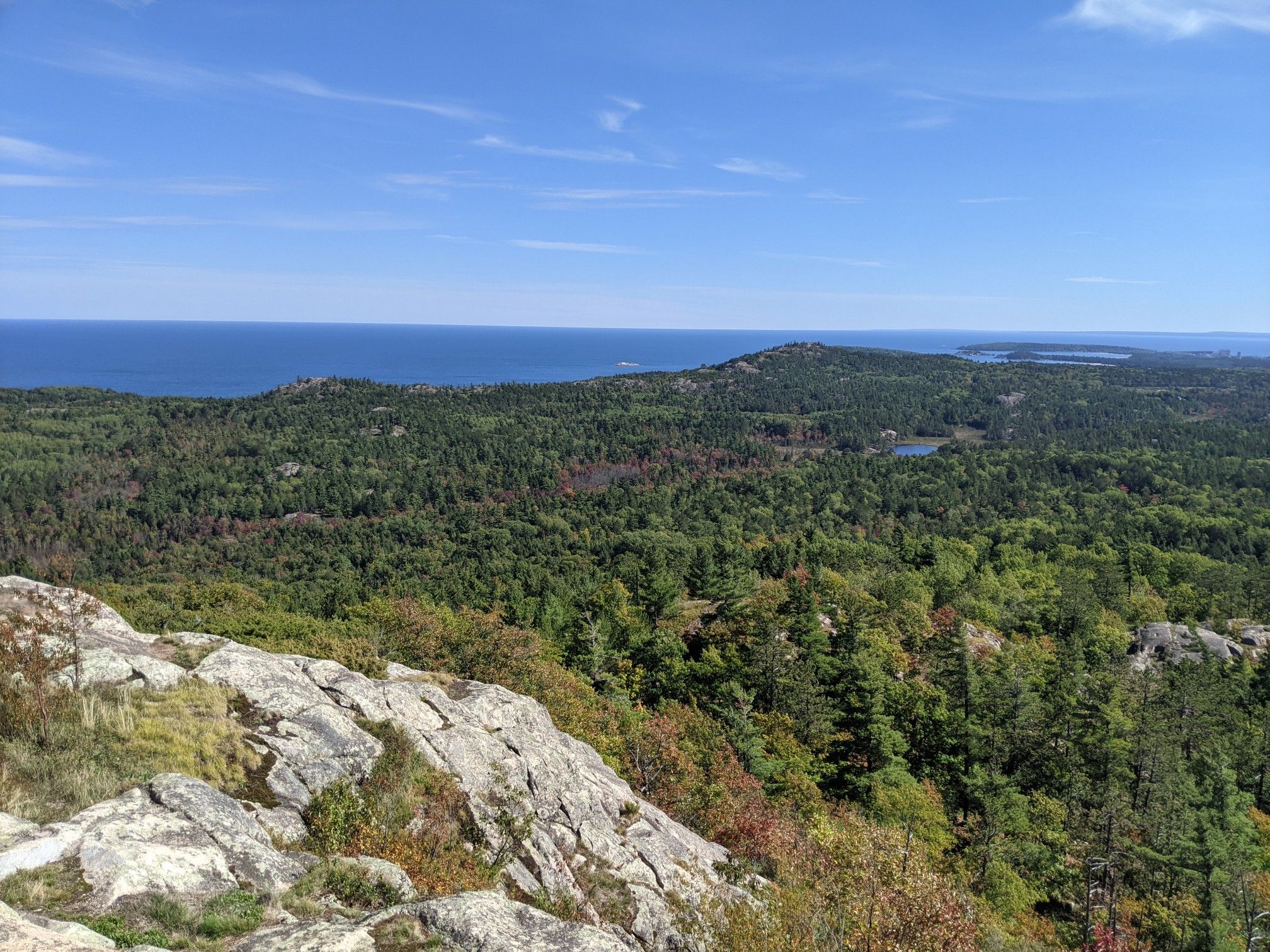 Panoramic view from a rocky outcrop overlooking a dense forest and distant ocean. - Hogback Mountain