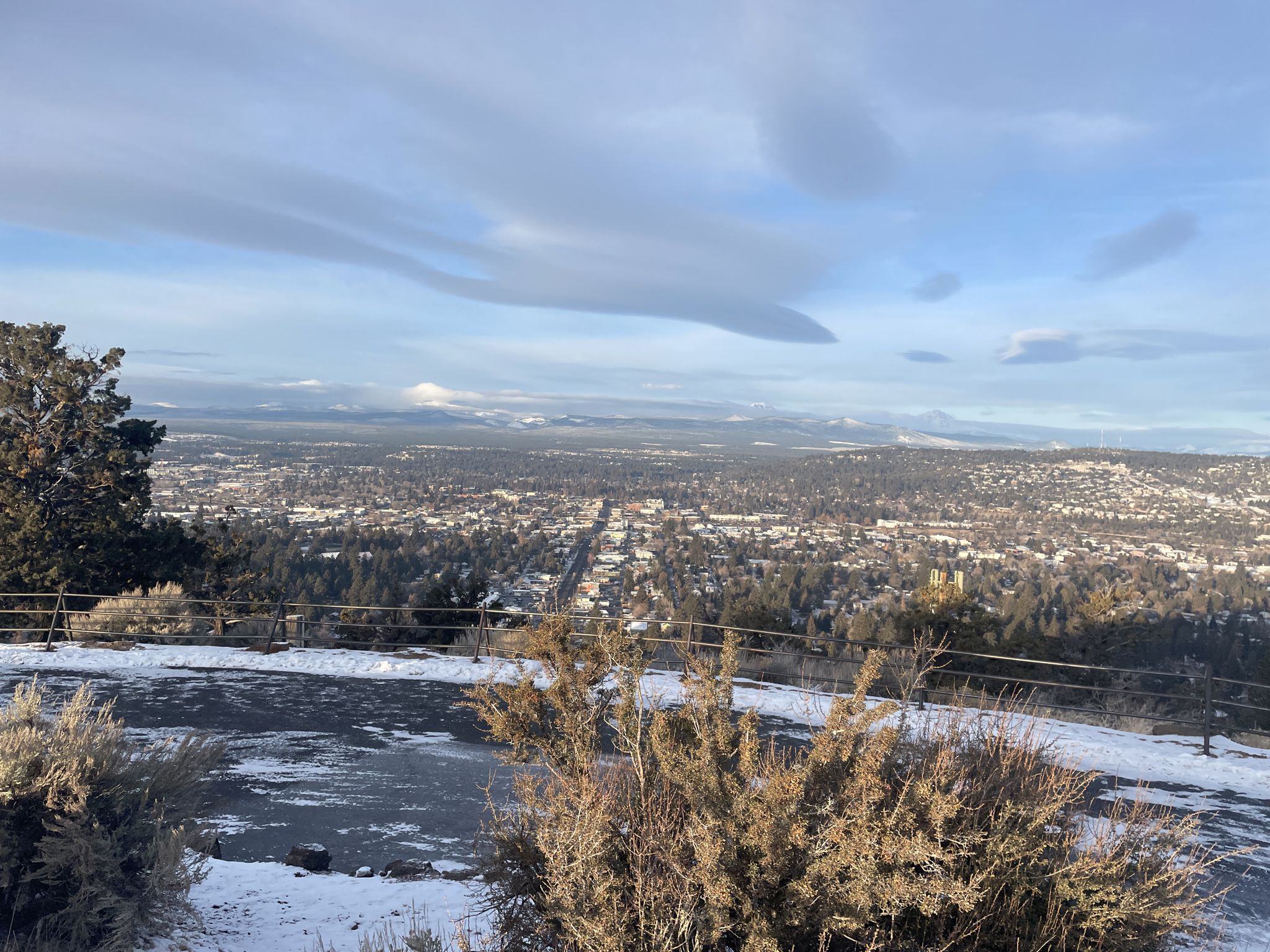 Panoramic view of a city and distant mountains under a cloudy sky. - Pilot Butte Nature Trail – View of Bend from Pilot Butte loop from Bend