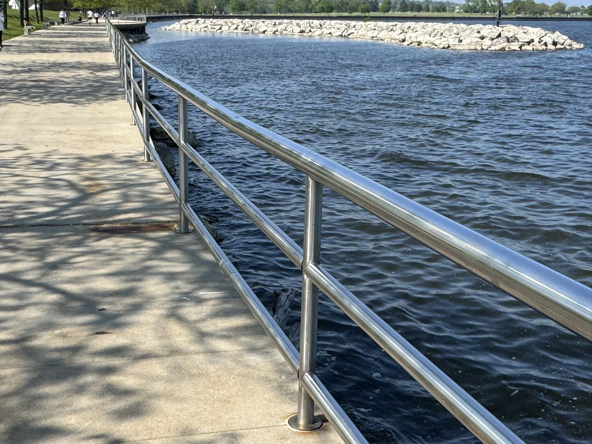 Sunny concrete path with metal railing next to water and rocky shore. - Oak Leaf Trail: Milwaukee River and Lake Loop