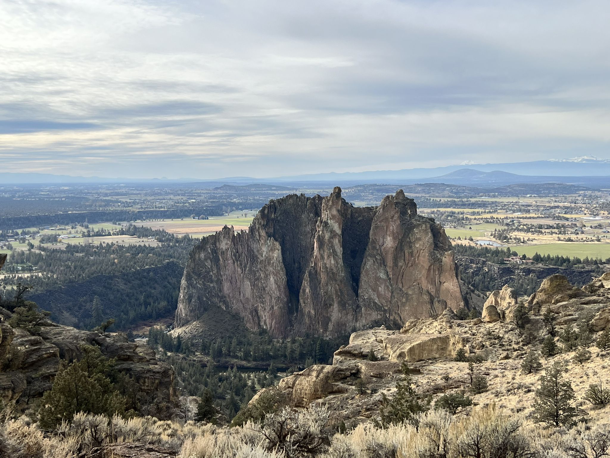 Majestic rock spires rise from a valley with distant mountains under a bright sky. - Crooked River – View of Smith Rock State Park loop from Smith Rock State Park