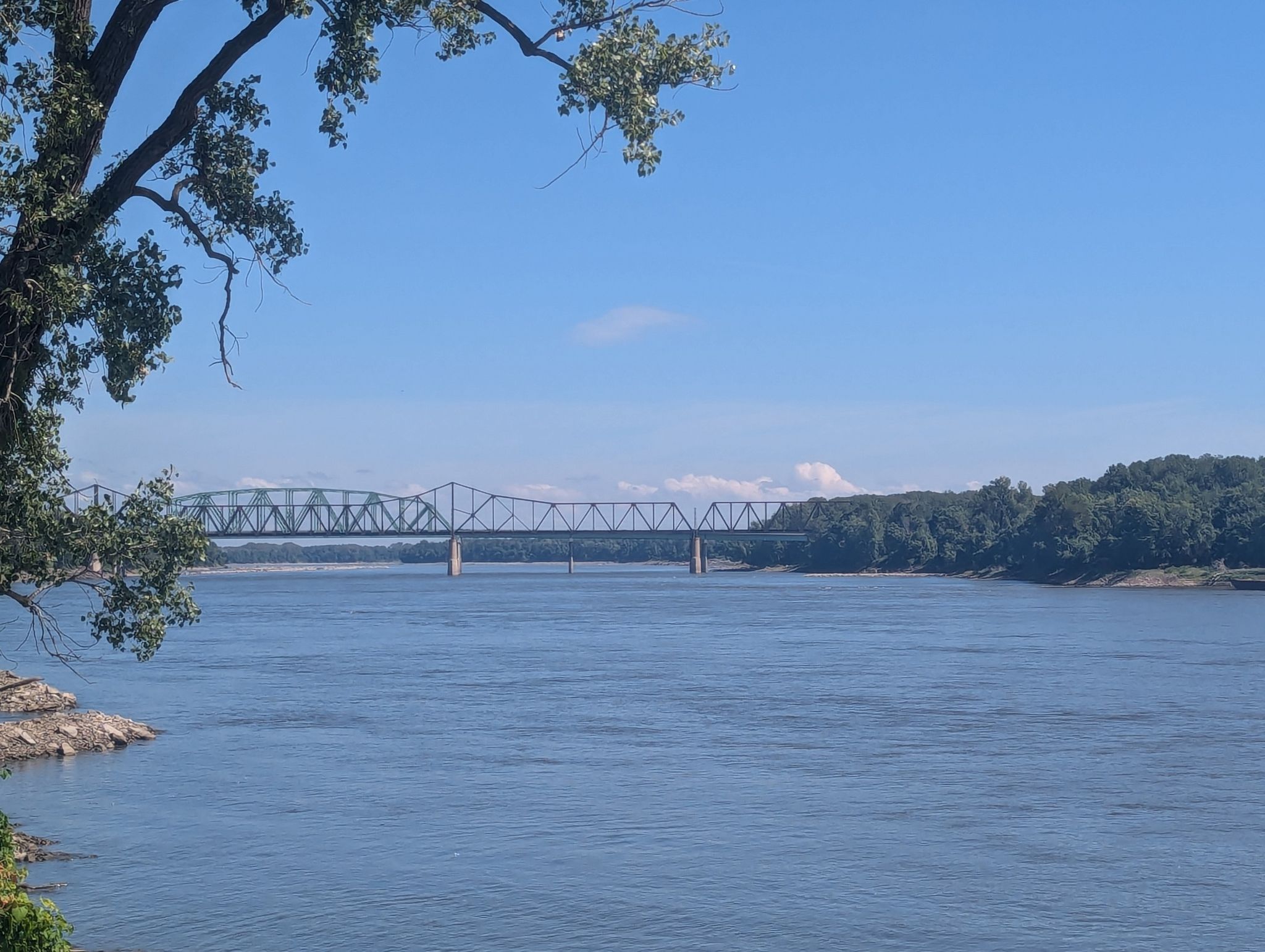 A large metal bridge spans a wide river under a clear blue sky. - Katy Trail and St. Charles Greenways Loop