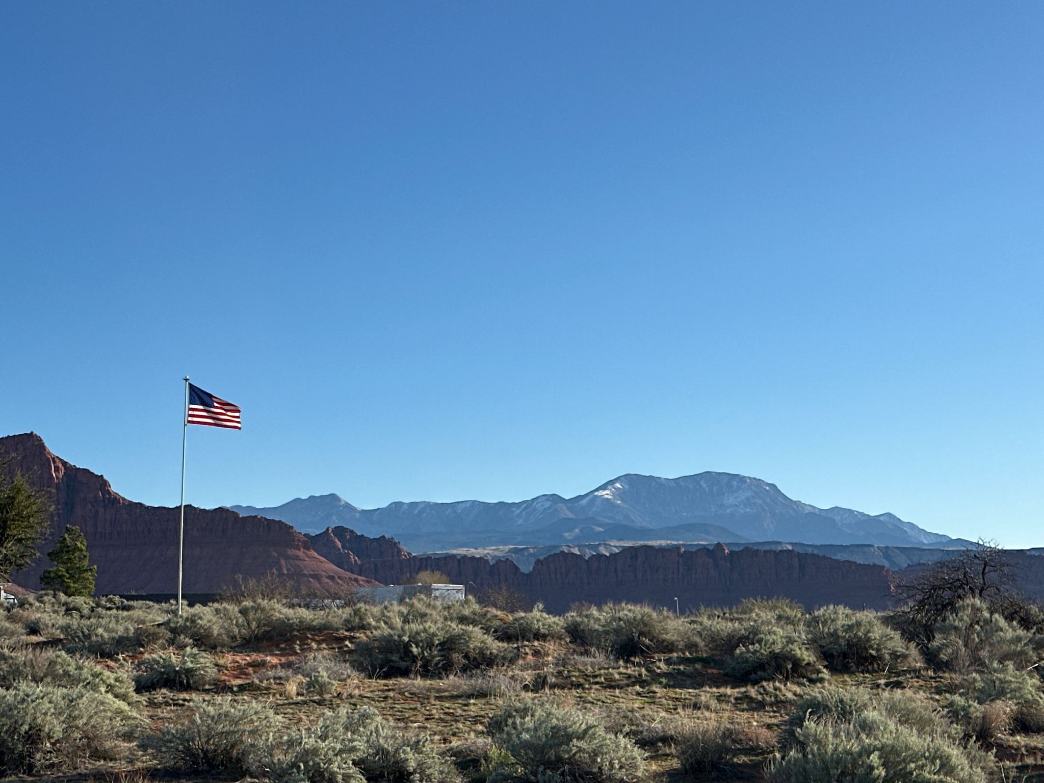American flag flying in a desert landscape with distant mountains under clear sky. - Tempi'po'op Trail Loop