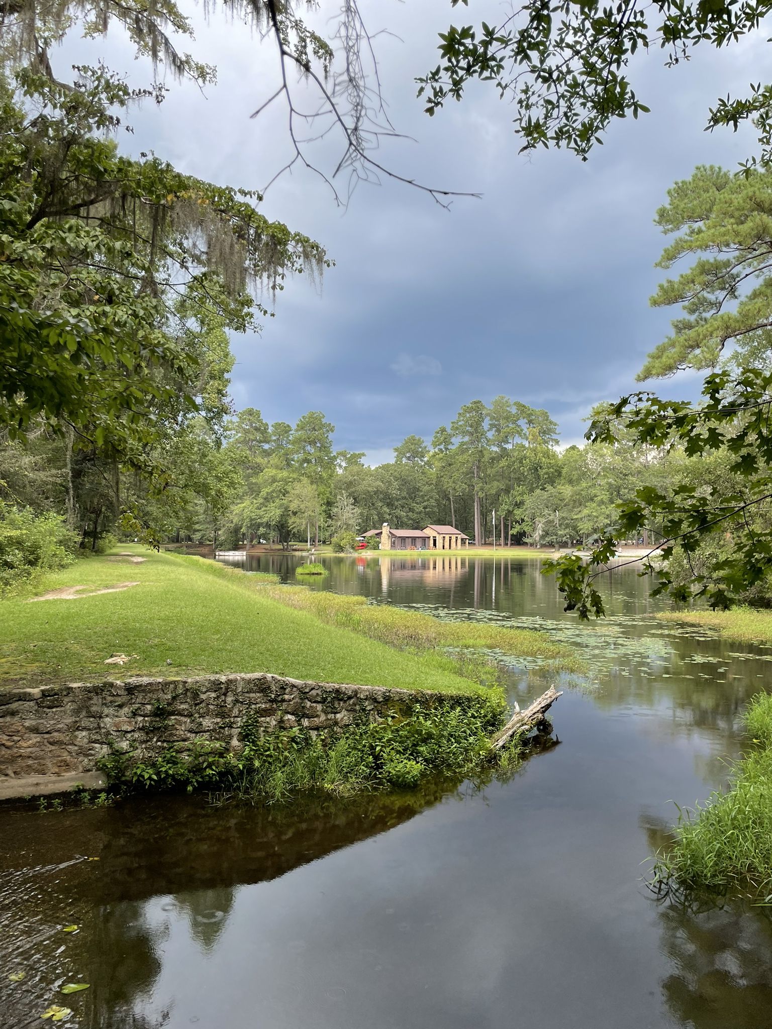 A tranquil lake with a distant building, surrounded by lush green trees. - Knot Trail